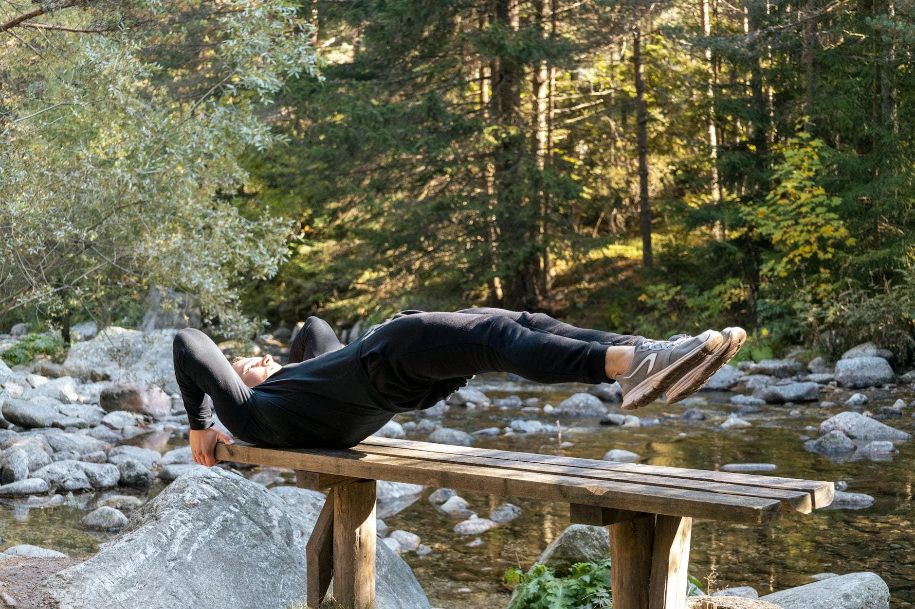 Man performing a core exercise on a bench by a serene river in a forest setting. - bodyweight exercises for beginners