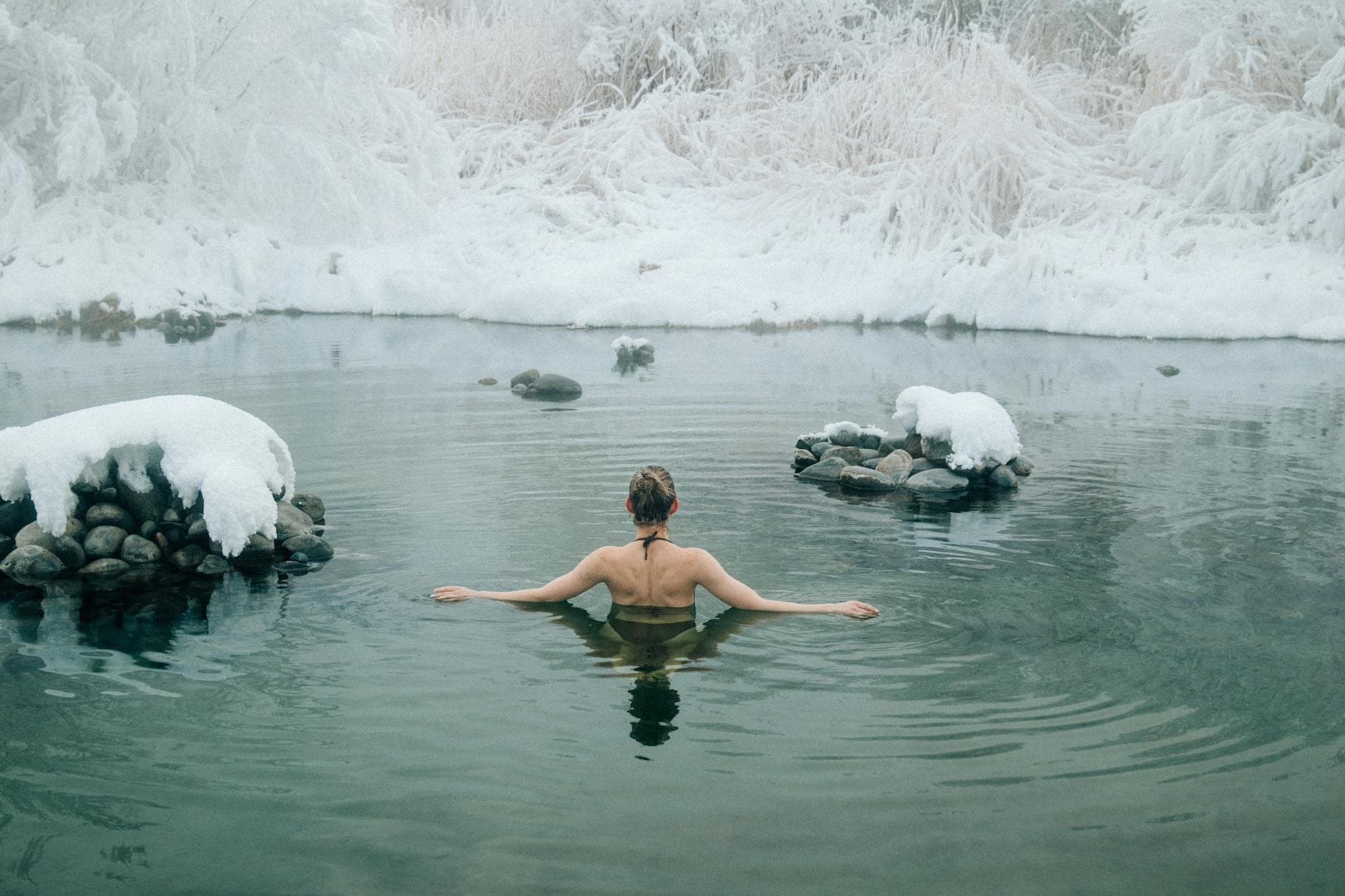 A young woman enjoying a swim in a tranquil winter lake surrounded by snow. - cold water swimming benefits