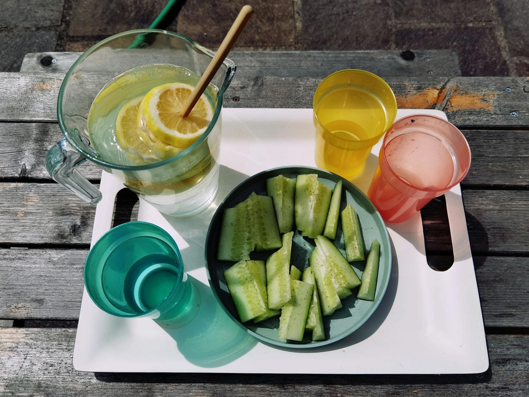 Outdoor shot of a summer picnic tray with lemon water and cucumber slices on a wooden table. - cucumber lemon detox water