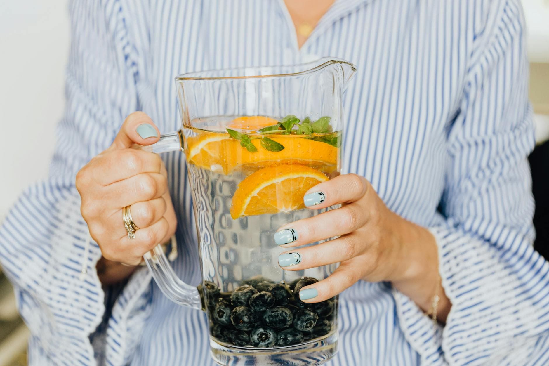 Close-up of infused water with oranges, blueberries, and mint in a glass pitcher. - detox water recipes