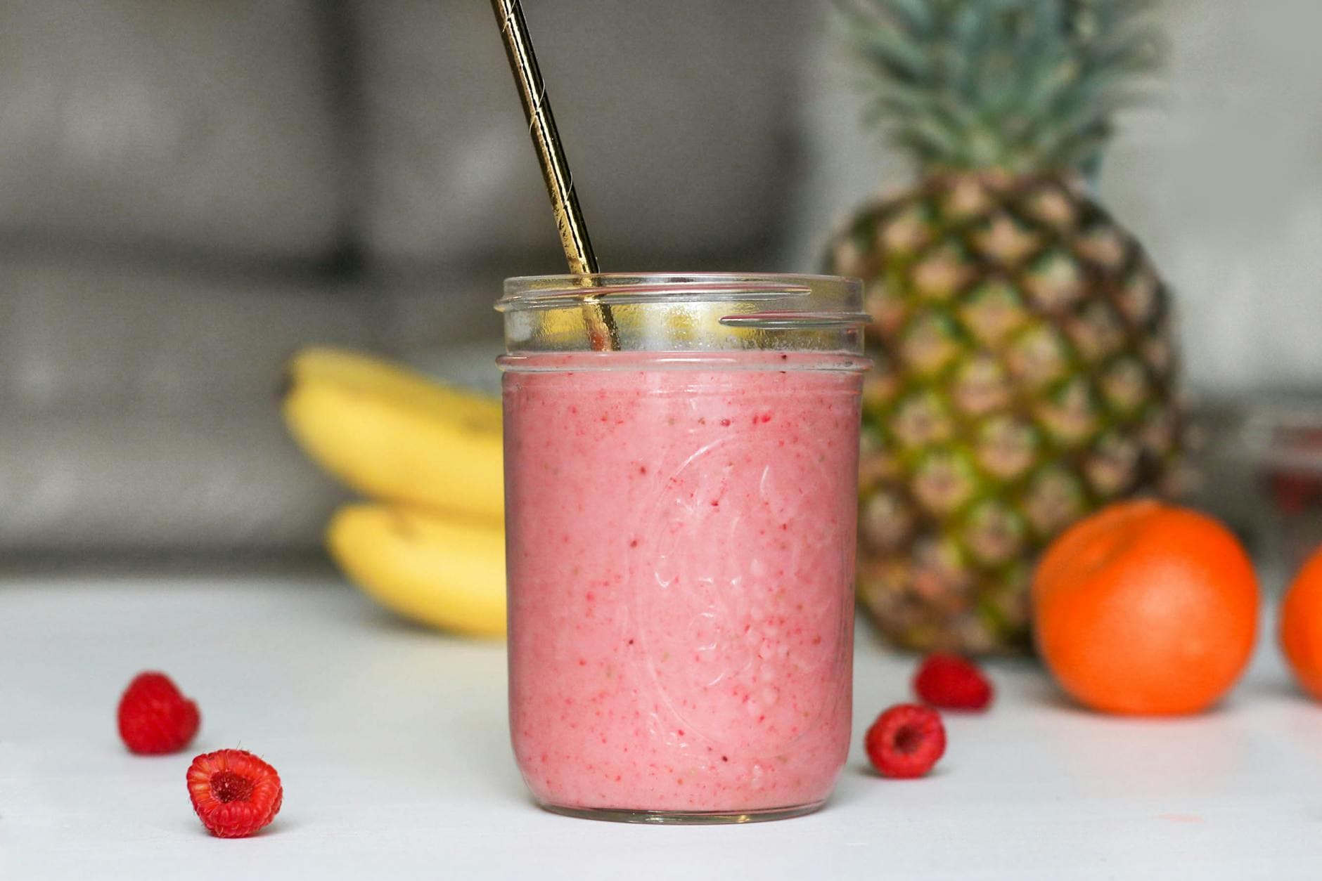 A refreshing pink smoothie made with bananas, raspberries, and tropical fruits in a glass jar. - energy boosting foods women