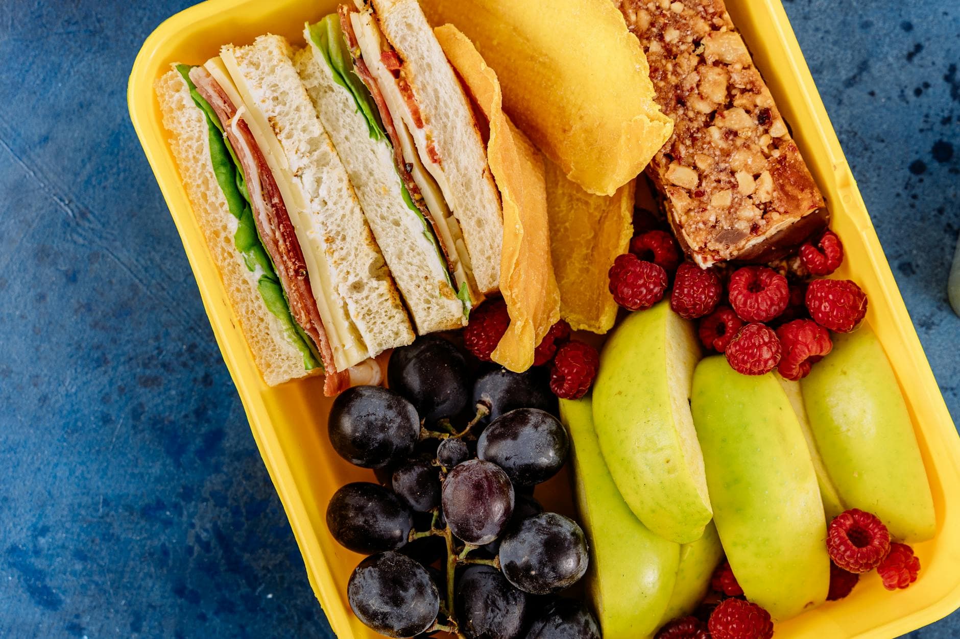 Vibrant lunchbox containing a sandwich, fresh fruits, and a snack bar, ideal for healthy meals. - quick healthy lunches