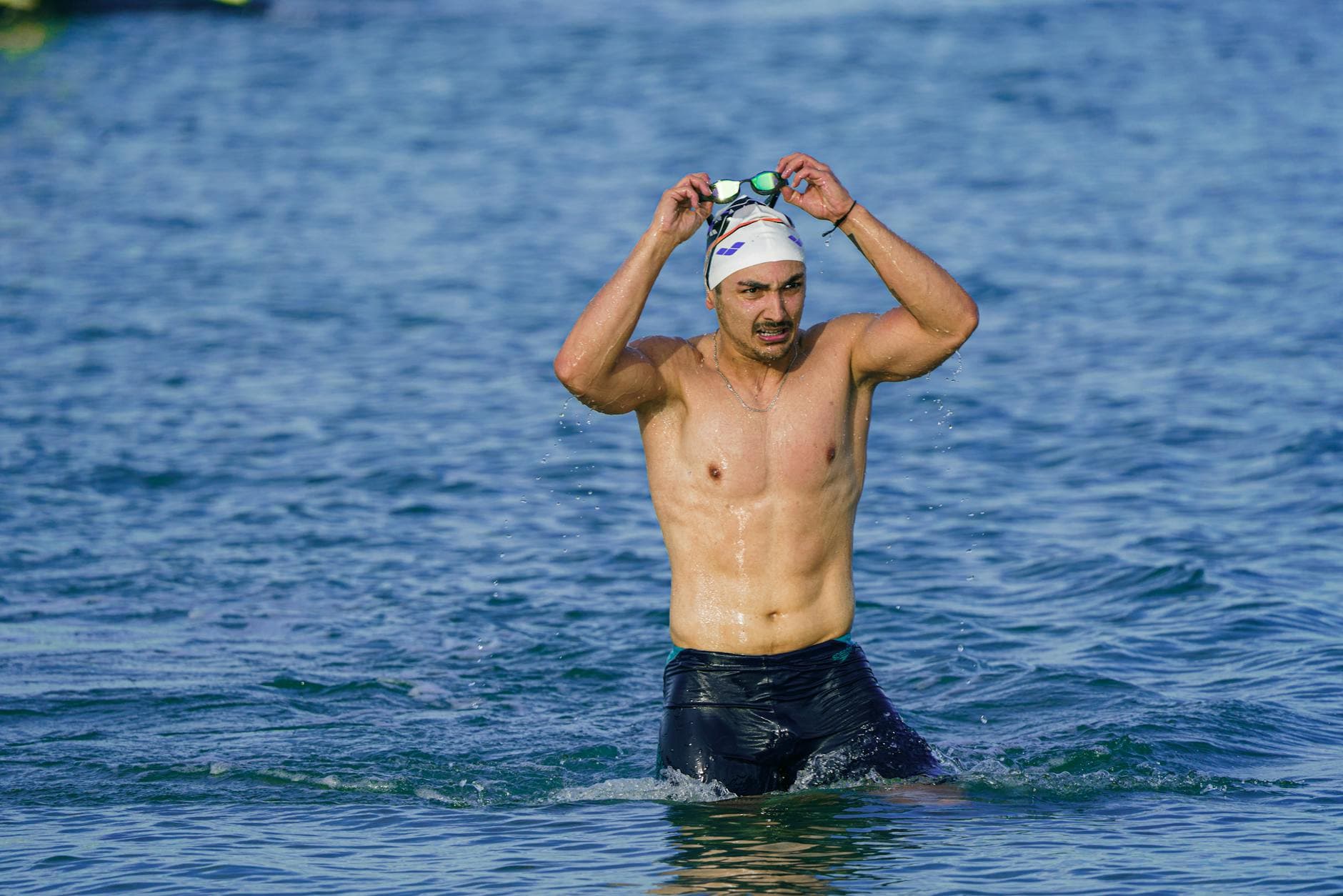 A male swimmer with goggles and swim cap emerges from the sea in Kuşadası, Türkiye. - swimming benefits for men