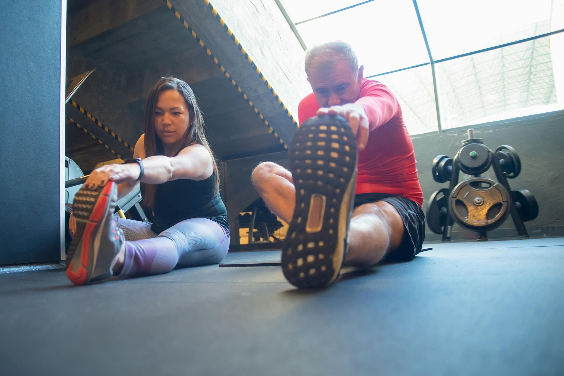 An elderly man and a woman doing stretching exercises on the floor of a gym, promoting a healthy lifestyle. - beginner stretching routine