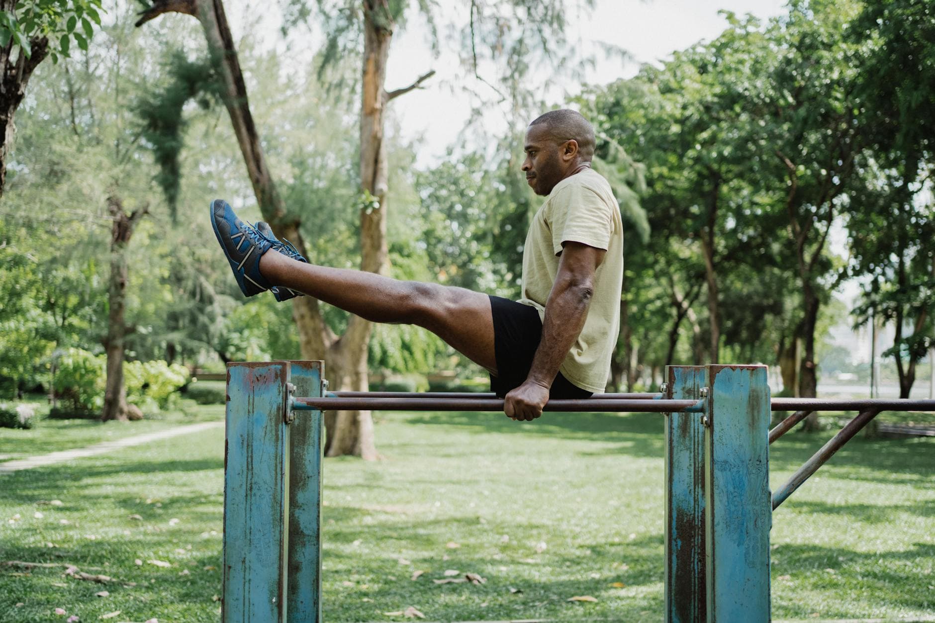 A man performing a leg raise on a dip bar in a sunny outdoor park setting. - best ab workout