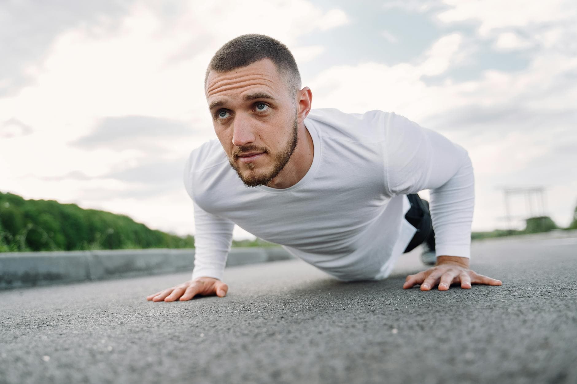 Focused man in sportswear doing push-ups on a road in a natural setting. - best core exercises