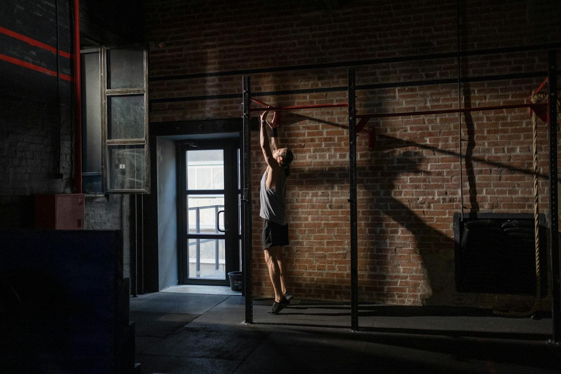 A man exercises on a pull-up bar in an industrial-style gym with brick walls, conveying fitness and dedication. - bodyweight arm exercises