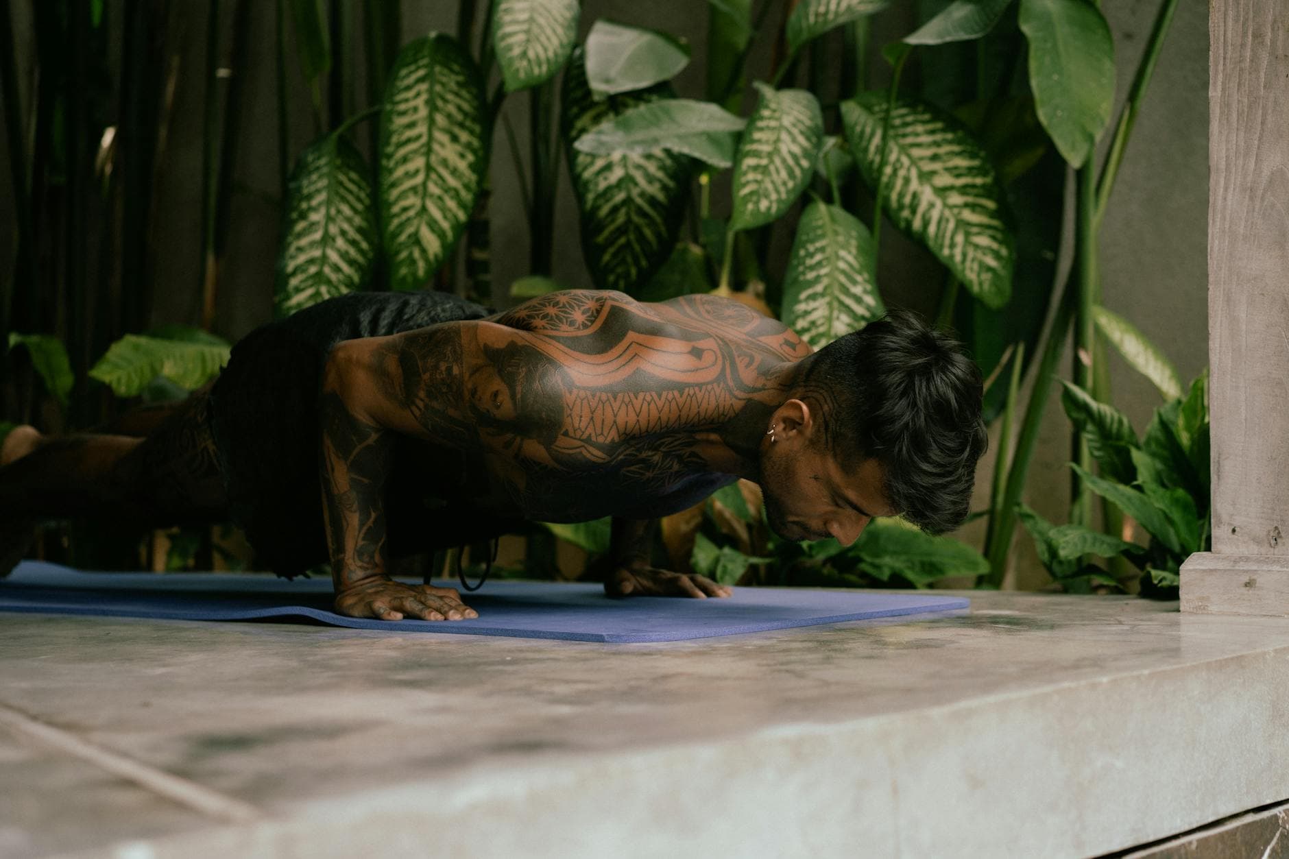 Man with tattoos performing yoga outdoors, showcasing strength and stamina on a mat. - bodyweight shoulder exercises