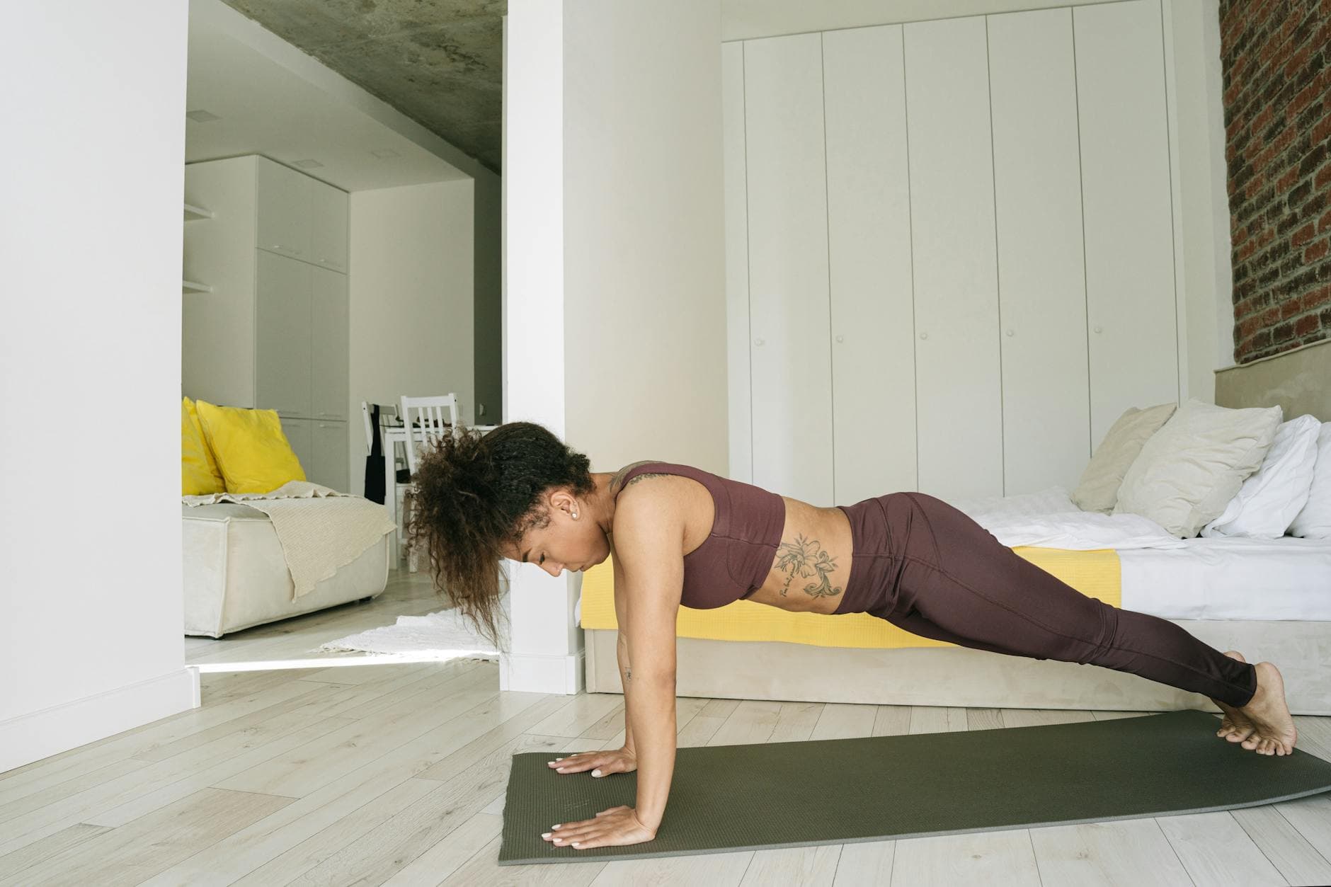Athletic woman in active wear practicing yoga in a modern bedroom setting, focusing on strength and flexibility. - bodyweight workouts home