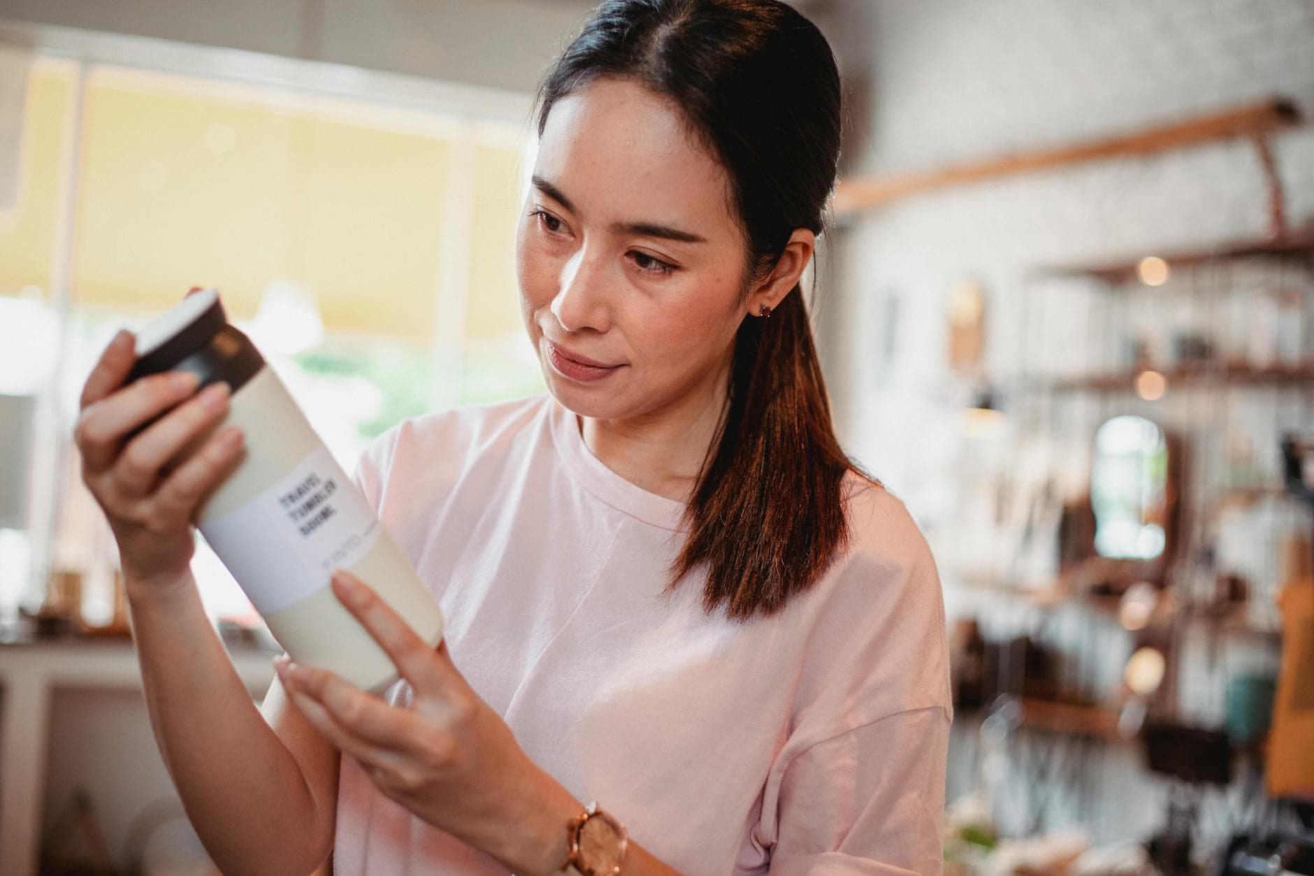 Crop young attentive ethnic shopper reading information on bottle of cosmetic product in store - buy natural skin care products