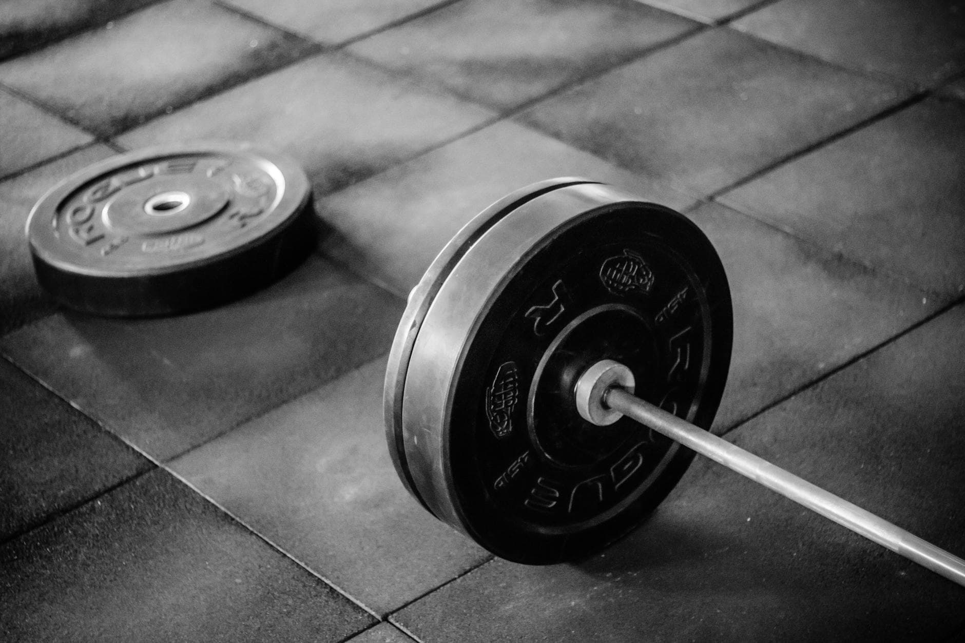 Grayscale image of heavy gym barbell and weights on rubber mat flooring. - crossfit workout plan