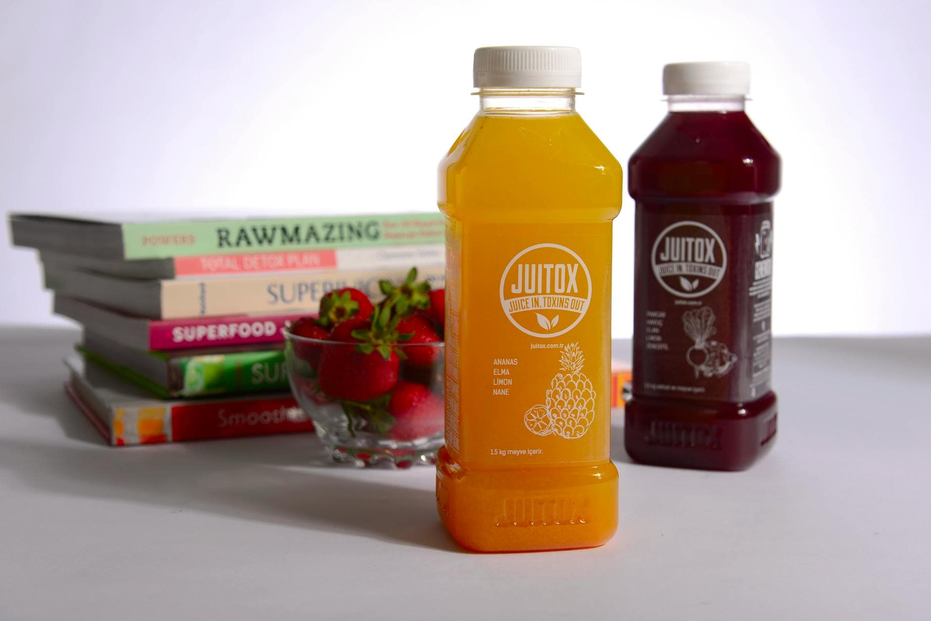 Colorful juice bottles surrounded by health-themed books and fresh strawberries. - detox drink recipes