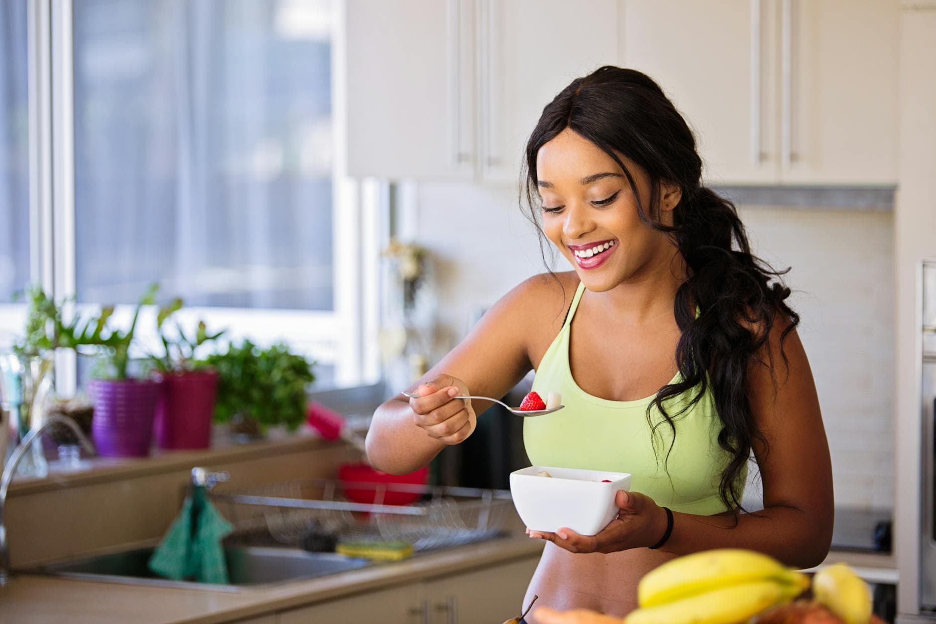 Smiling woman eating a nutritious fruit bowl in a bright kitchen setting. - fat burning foods
