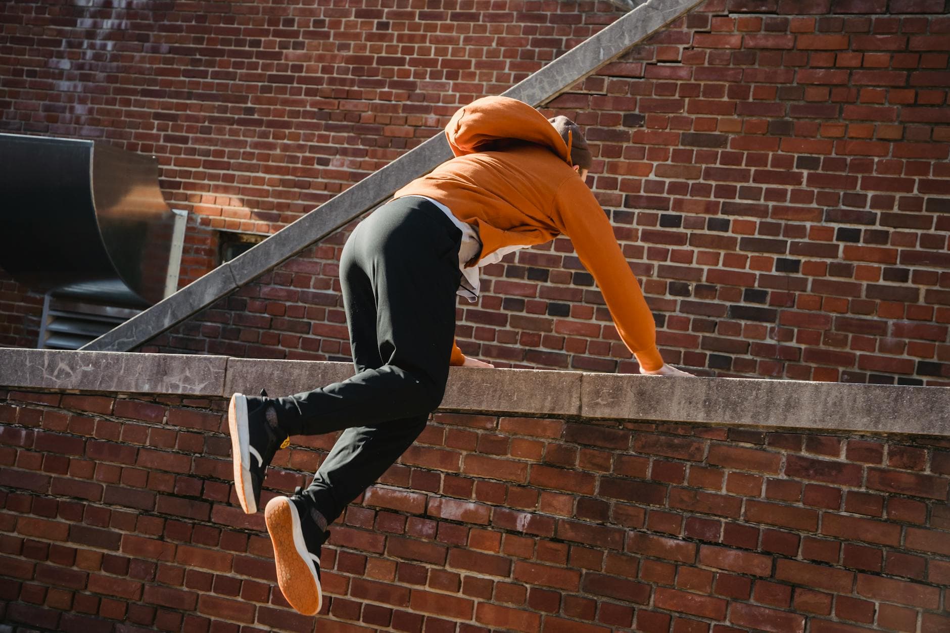 Back view anonymous male tracer in casual wear performing tricks while practicing parkour on brick building - free running beginners