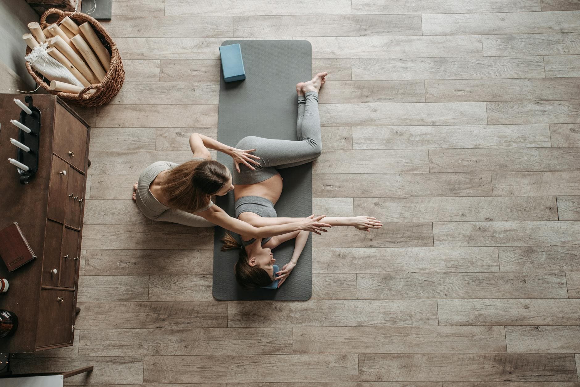 Overhead view of a yoga instructor helping a woman stretch on a mat during an indoor session. - full body stretch