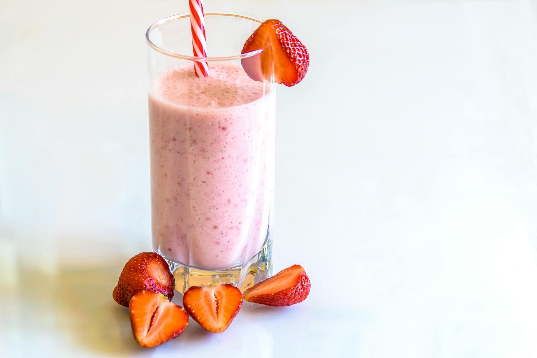 Delicious strawberry smoothie in a glass with fresh strawberries and a striped straw on a light background. - high fiber foods