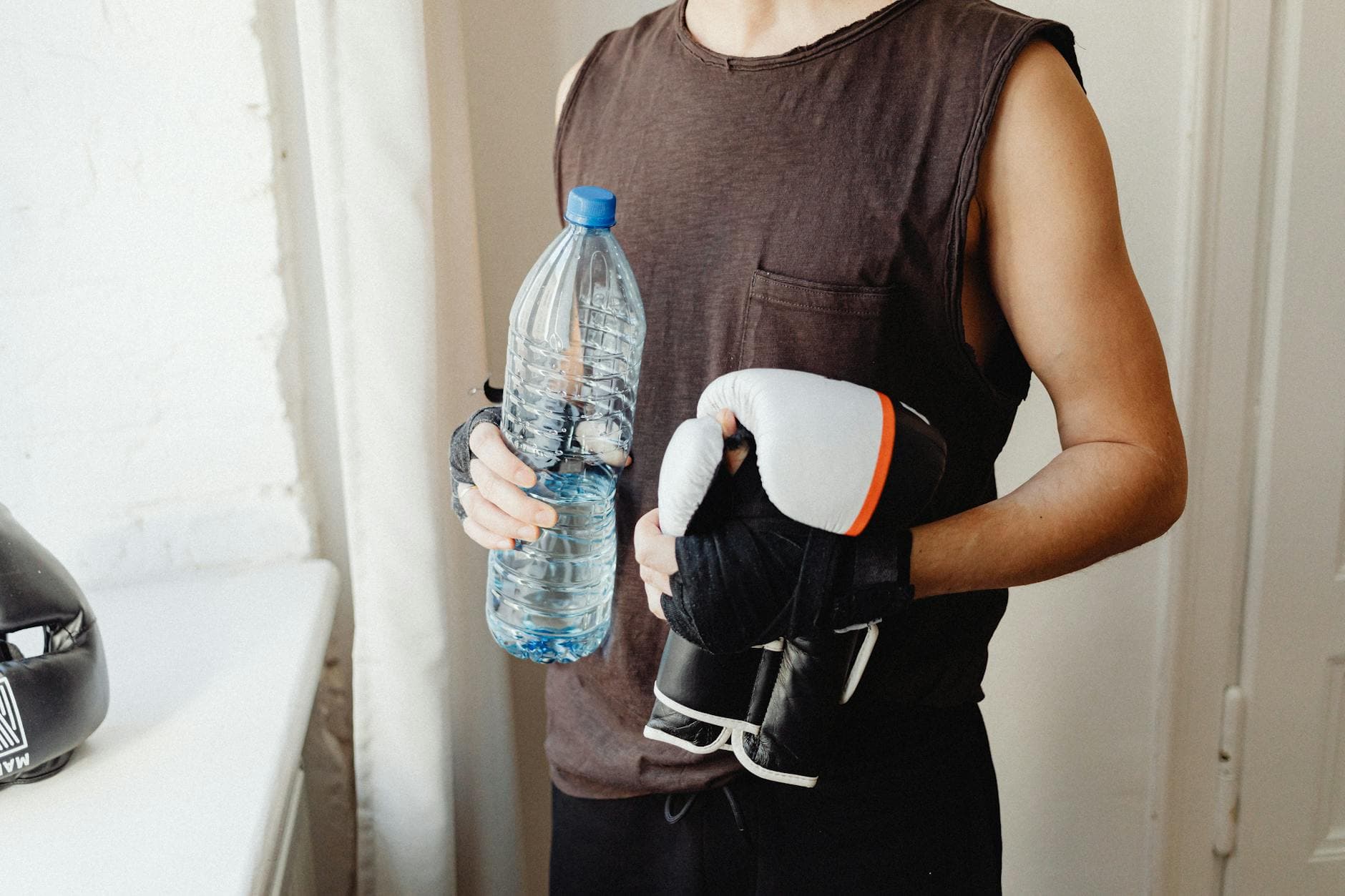 A male boxer holding a water bottle and boxing gloves, representing a healthy lifestyle. - hydration hacks