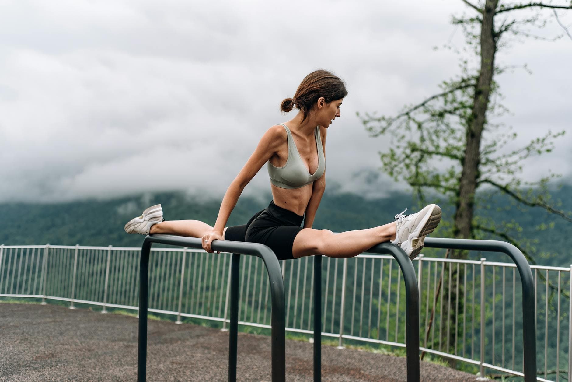 A woman in sportswear performing a split outdoors on metal bars, showcasing flexibility and strength. - lower body exercises