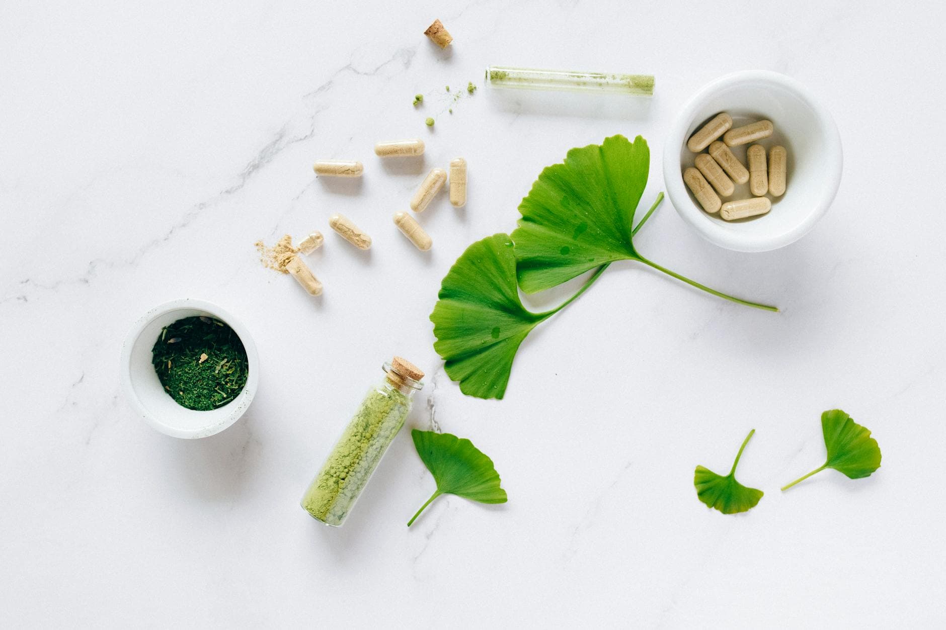 Flat lay of herbal supplements with ginkgo leaves on marble surface, emphasizing natural health remedies. - magnesium glycinate benefits