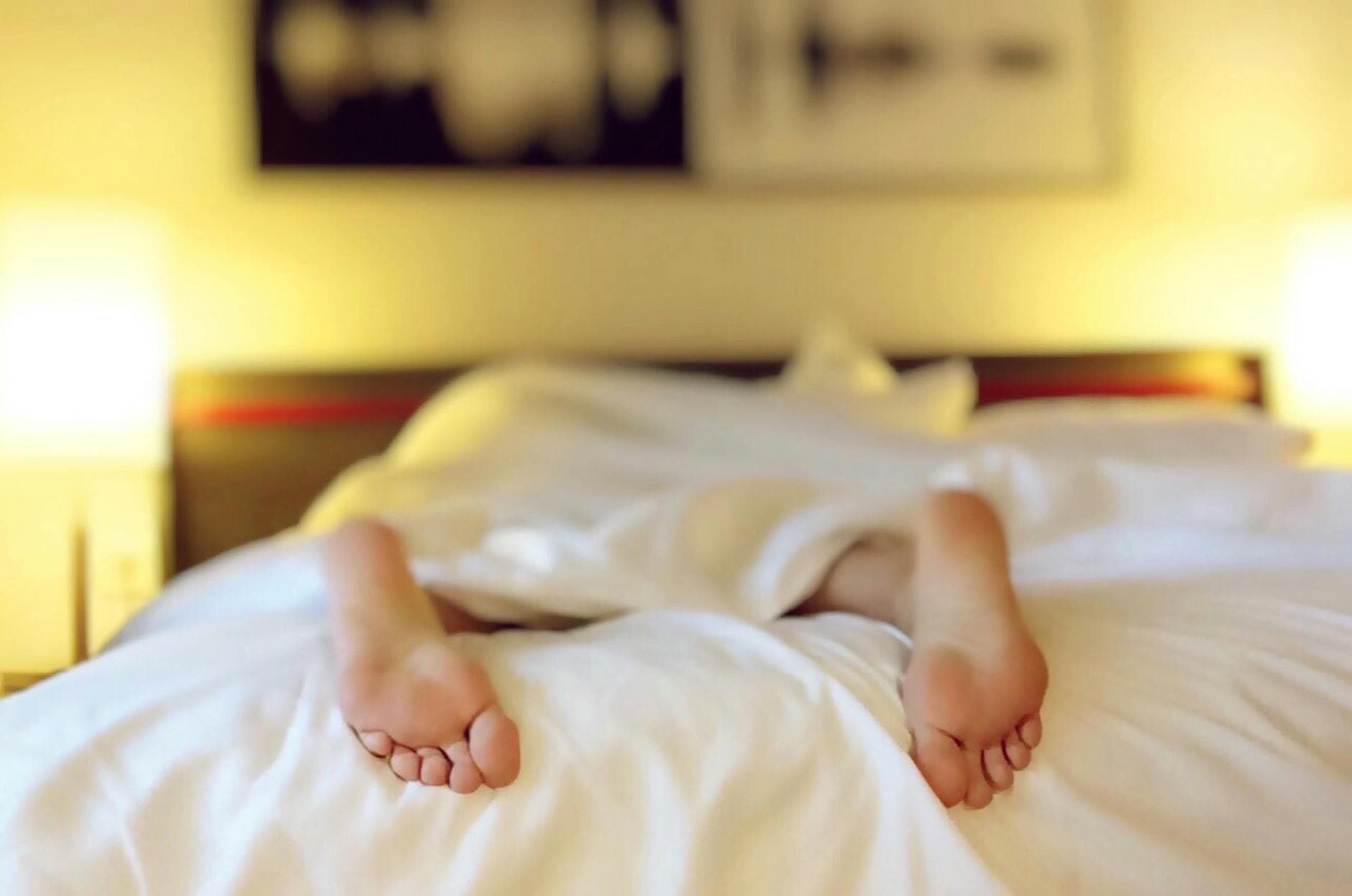 A person relaxing on a bed with feet under white sheets, conveying serenity. - mindfulness for sleep