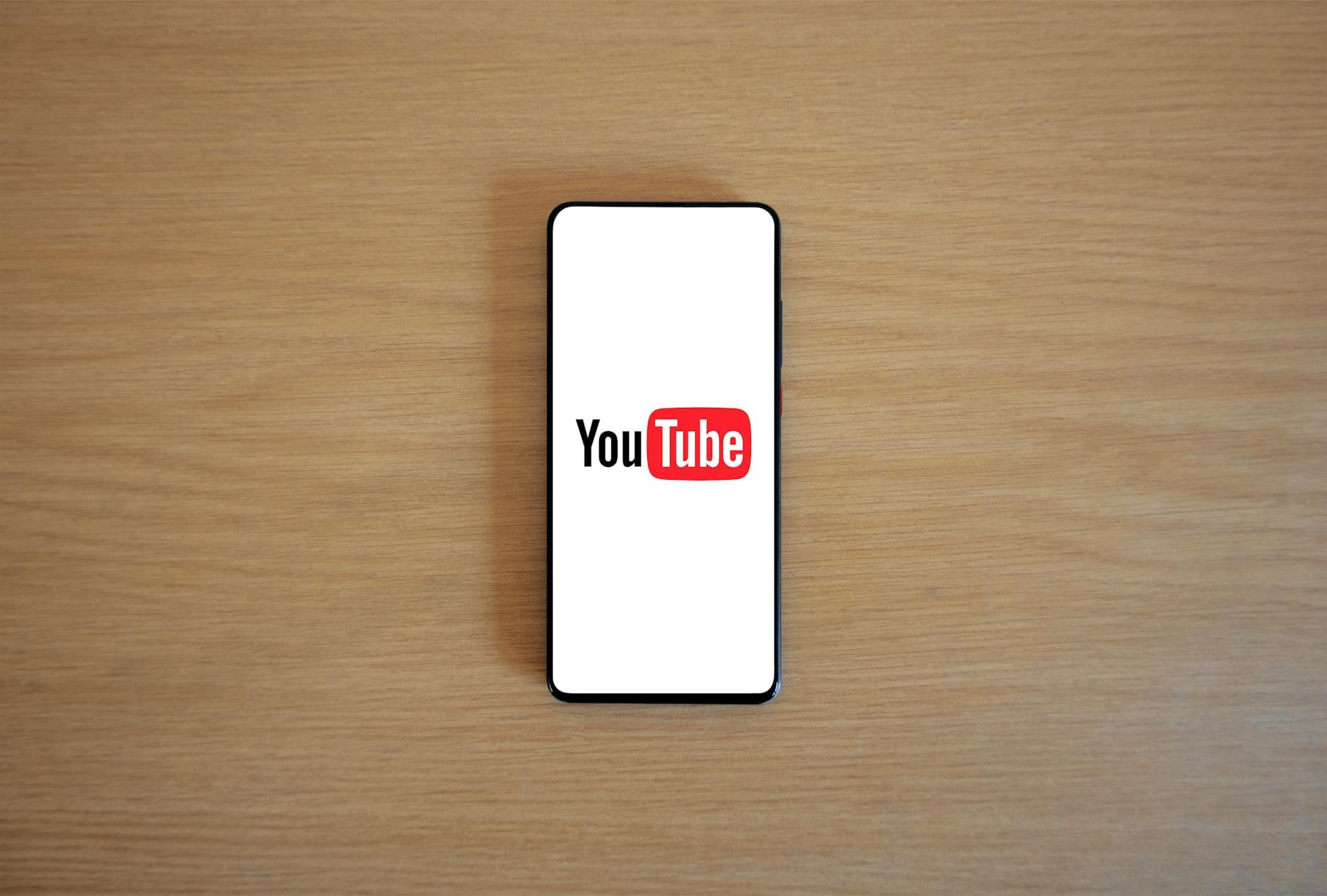 Top view of smartphone displaying YouTube logo on a wooden surface, showcasing modern technology. - morning yoga youtube