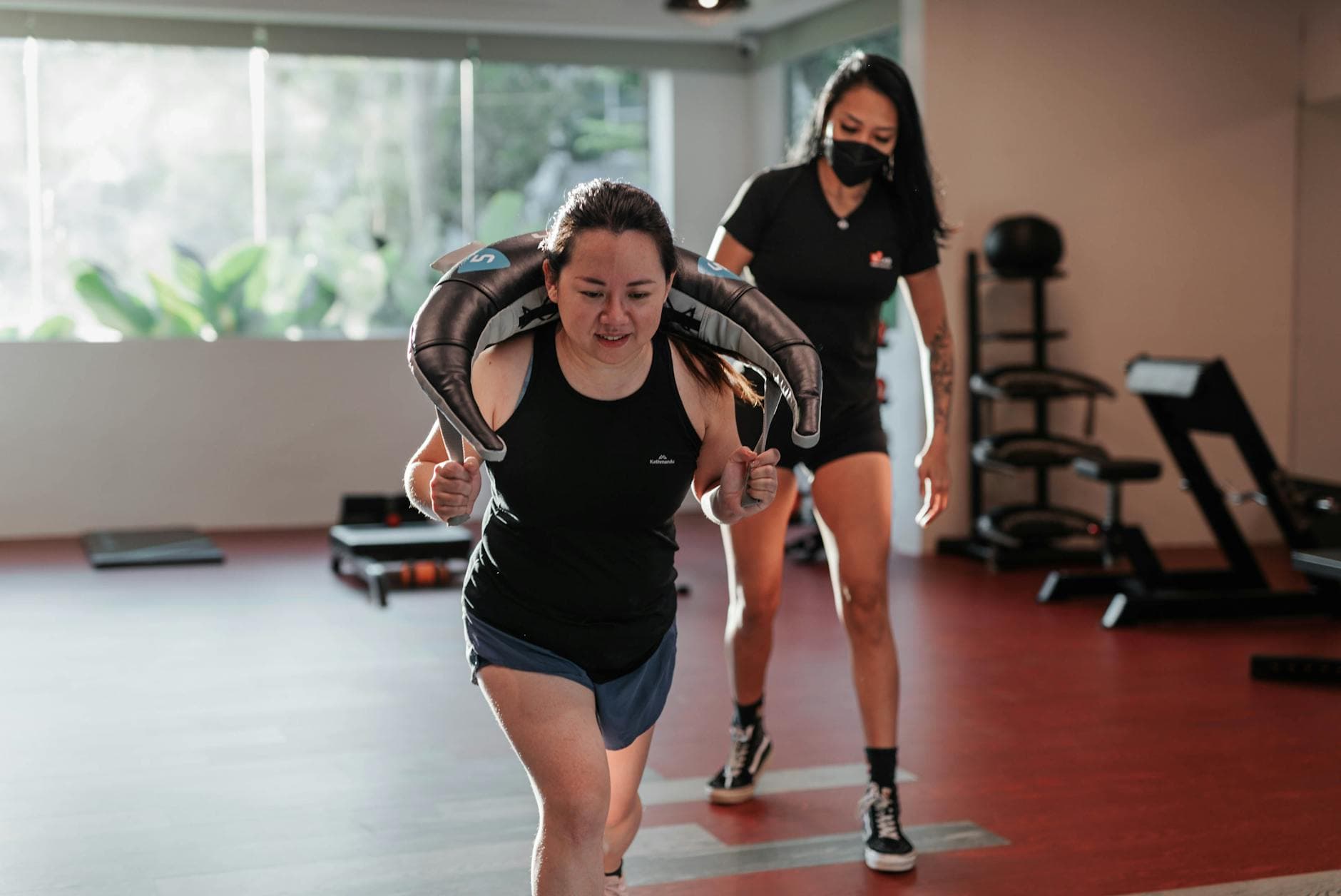 Two women focused on strength training in a Singapore gym with a personal trainer. - planet fitness workout