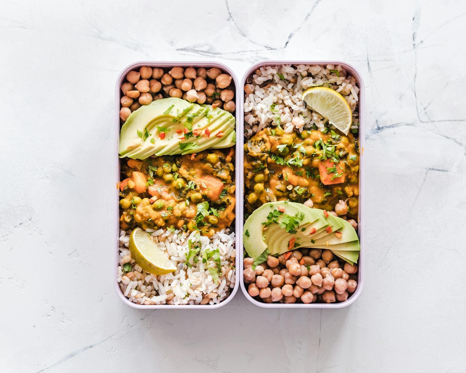 Delicious vegan lunchboxes featuring chickpeas, rice, avocado, and curry on a white background. - protein fiber foods