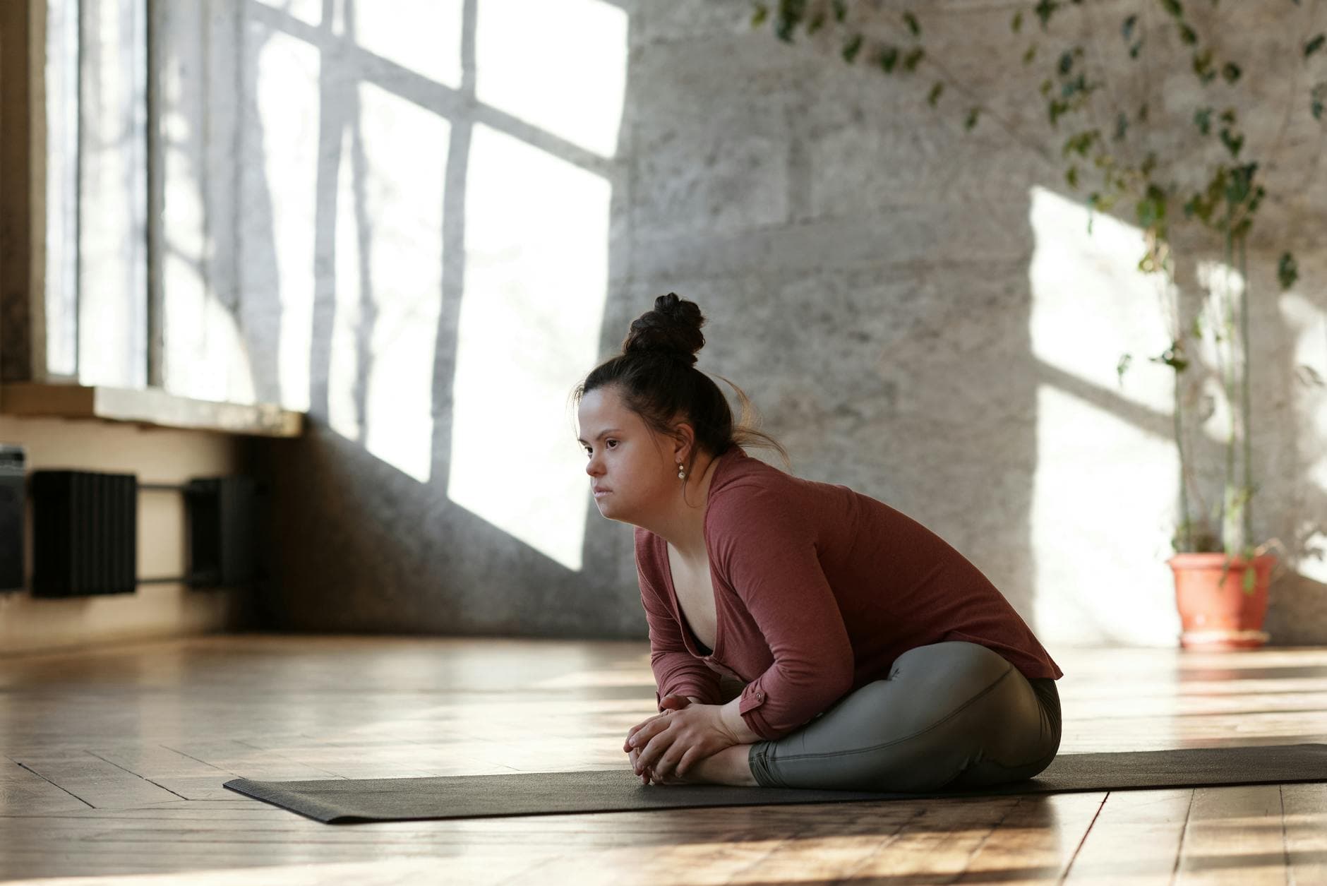 A woman with Down syndrome sits on a yoga mat indoors in a relaxed yoga pose. - quick morning yoga