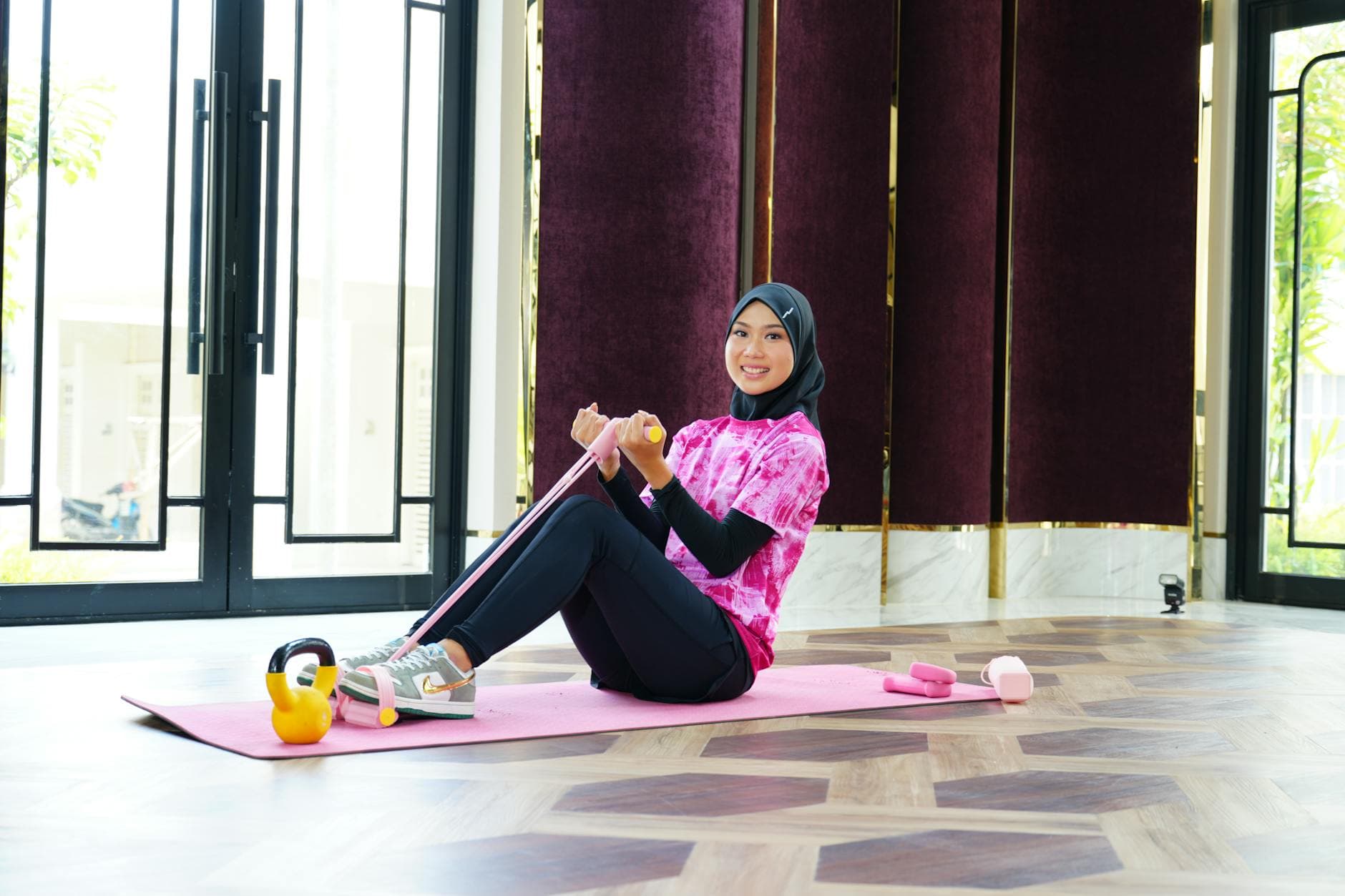 A woman in sporty attire and hijab exercises indoors using a resistance band, showcasing fitness and fashion. - spring calorie burning hikes