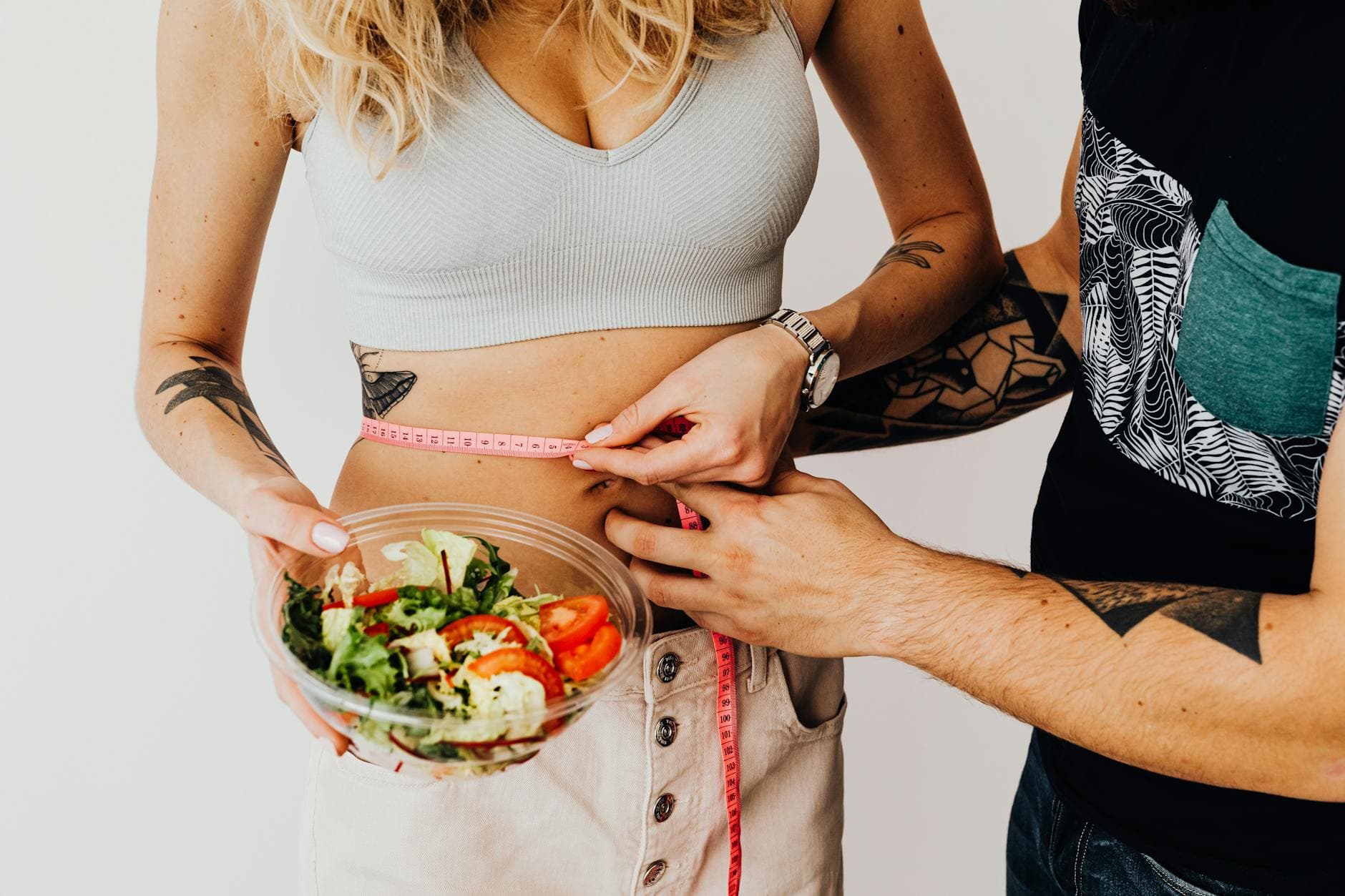 A couple measuring waistline with a tape and holding a fresh salad bowl, focusing on fitness and weight loss. - spring diet reset