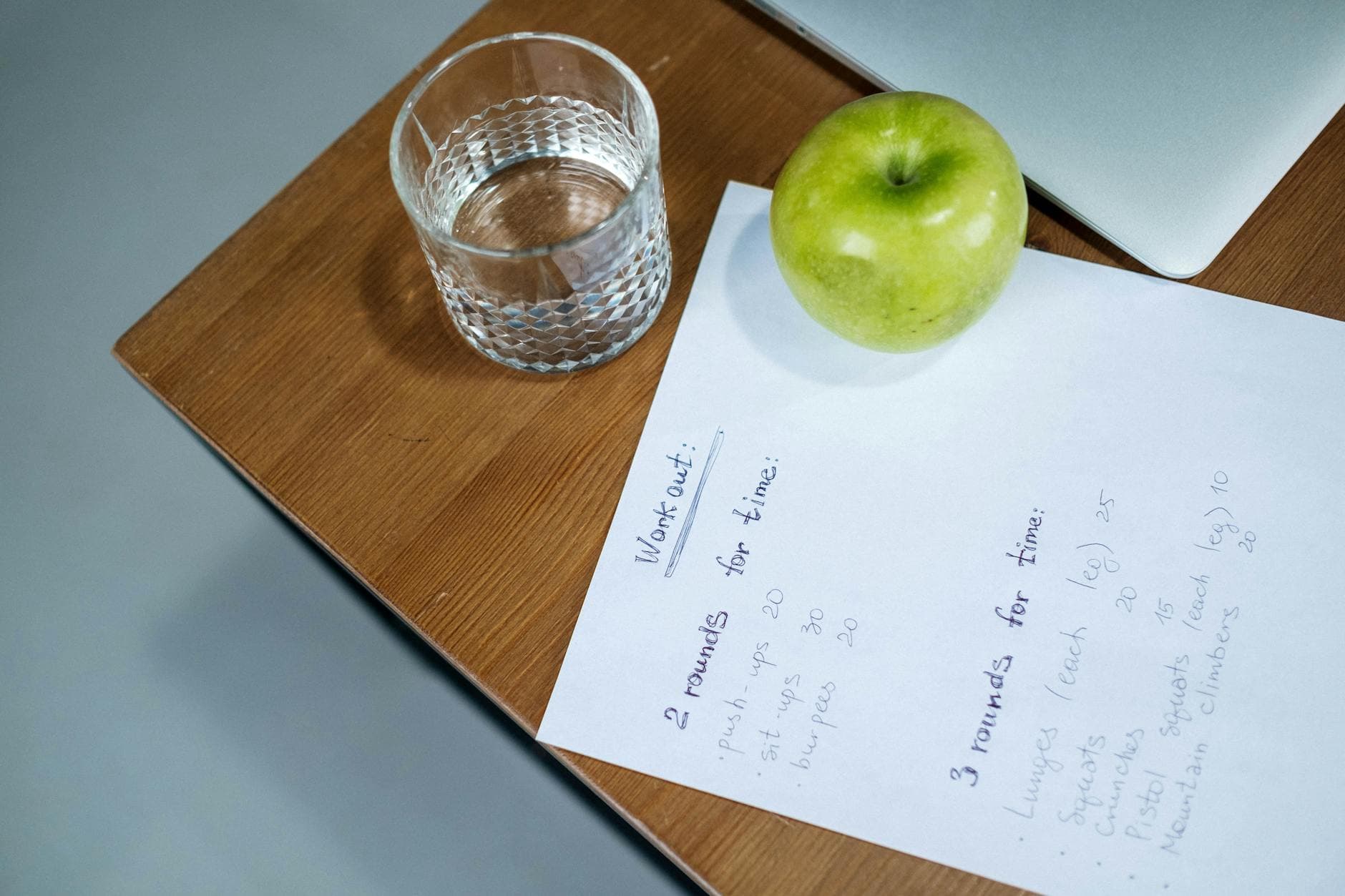 A green apple, glass of water, and workout plan on a wooden desk symbolize healthy living. - spring workout plan