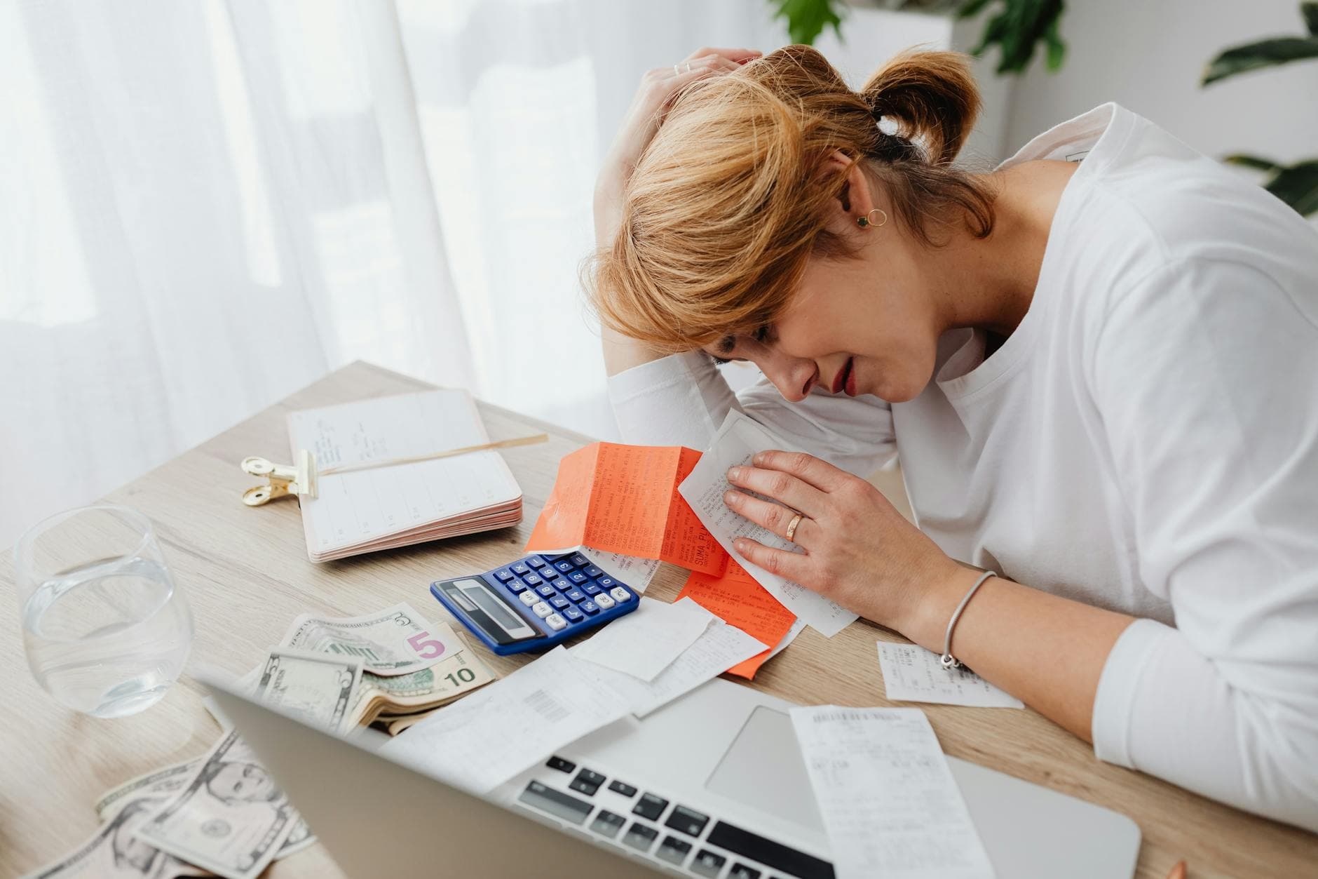 A woman overwhelmed with finances, surrounded by bills, calculator, and cash at home. - stress management techniques