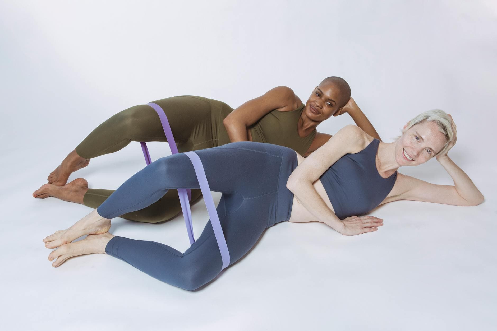Two diverse women in activewear stretching with resistance bands during a studio workout session. - stretching exercises