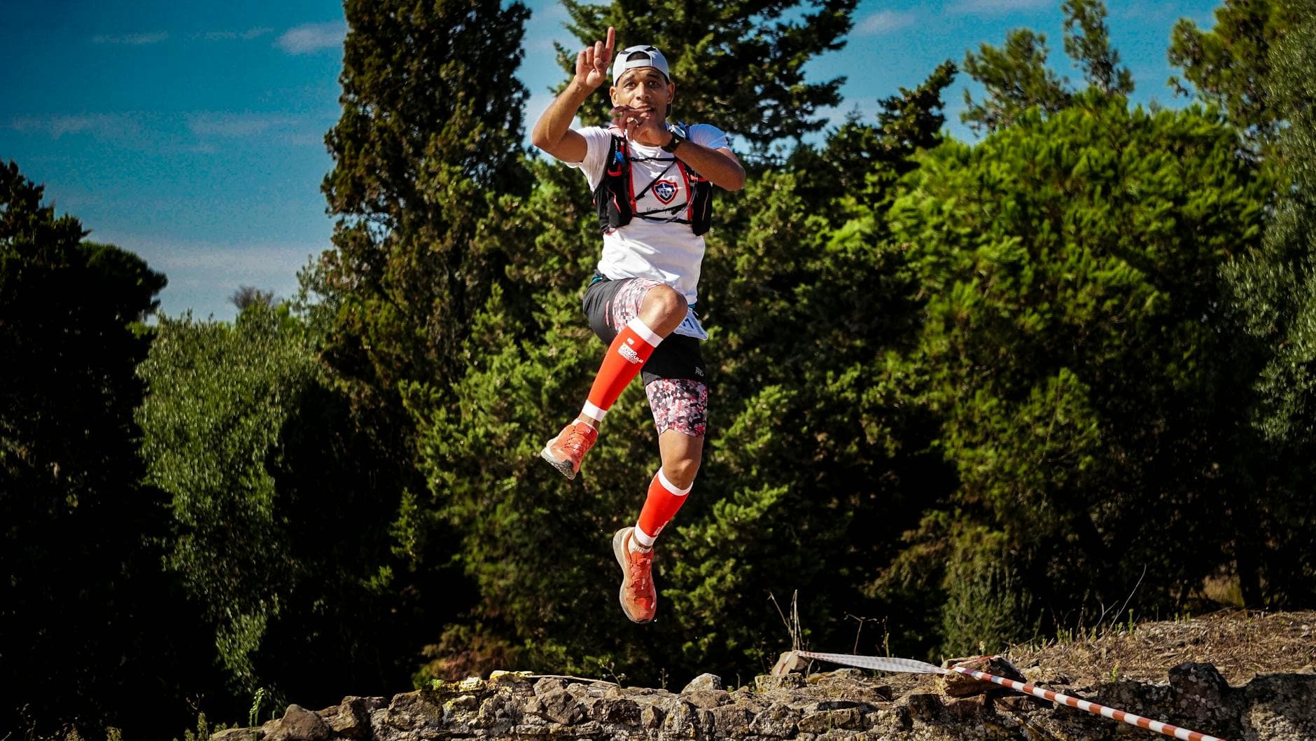 Energetic athlete jumps mid-air against a lush forest backdrop outdoors. - trail running beginners