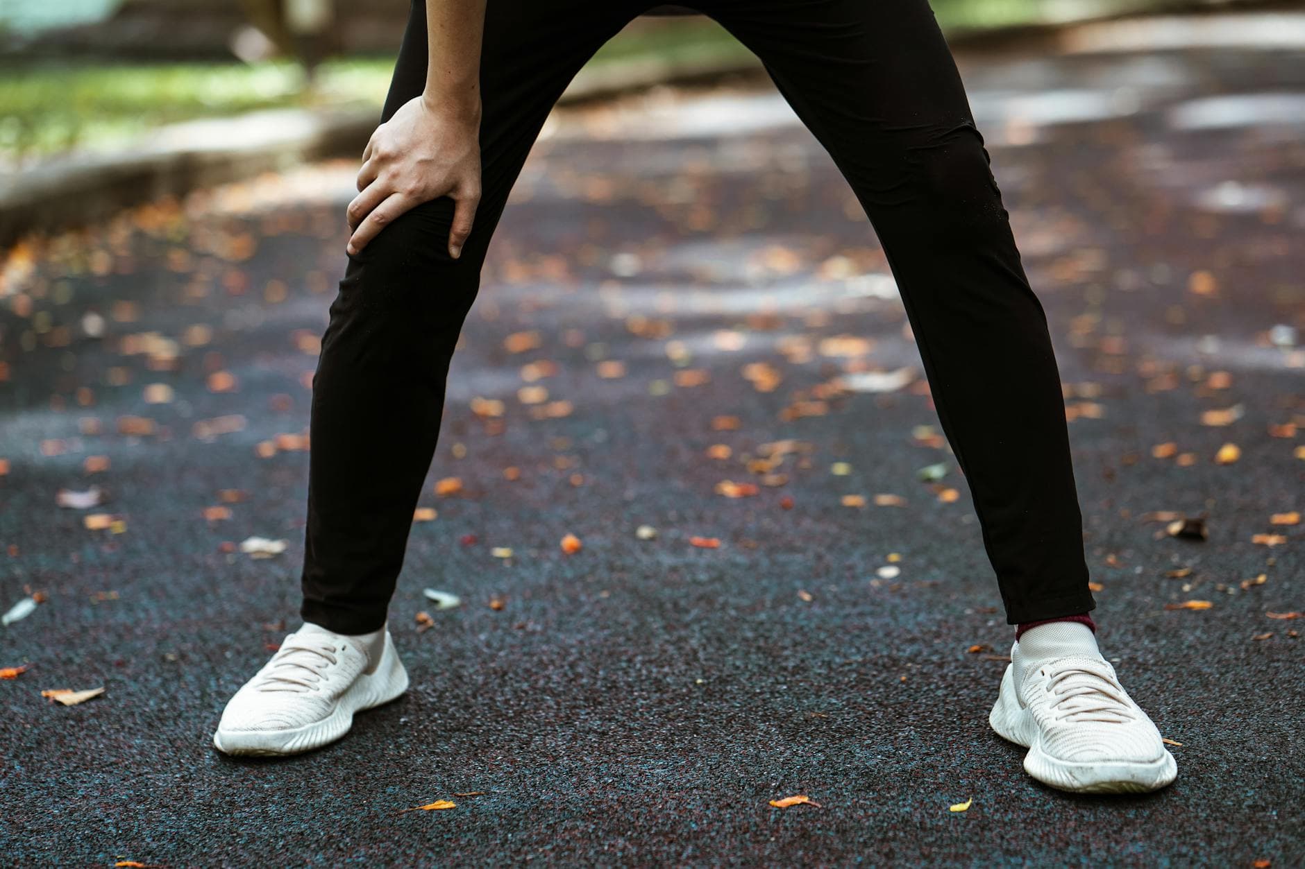 Legs of anonymous runner in white sneakers and black leggings taking breath after running leaning on knee - knee pain relief exercises