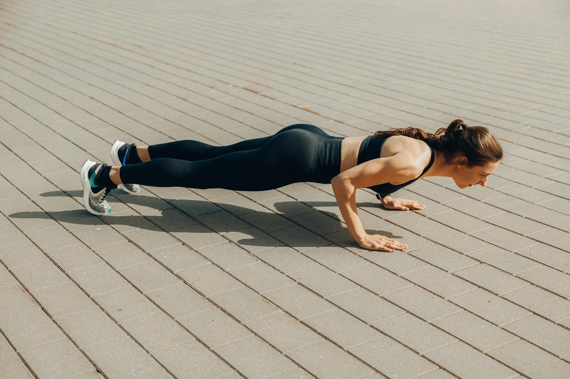 Woman performing a push-up exercise outdoors in sportswear, promoting fitness and a healthy lifestyle. - outdoor bodyweight workout