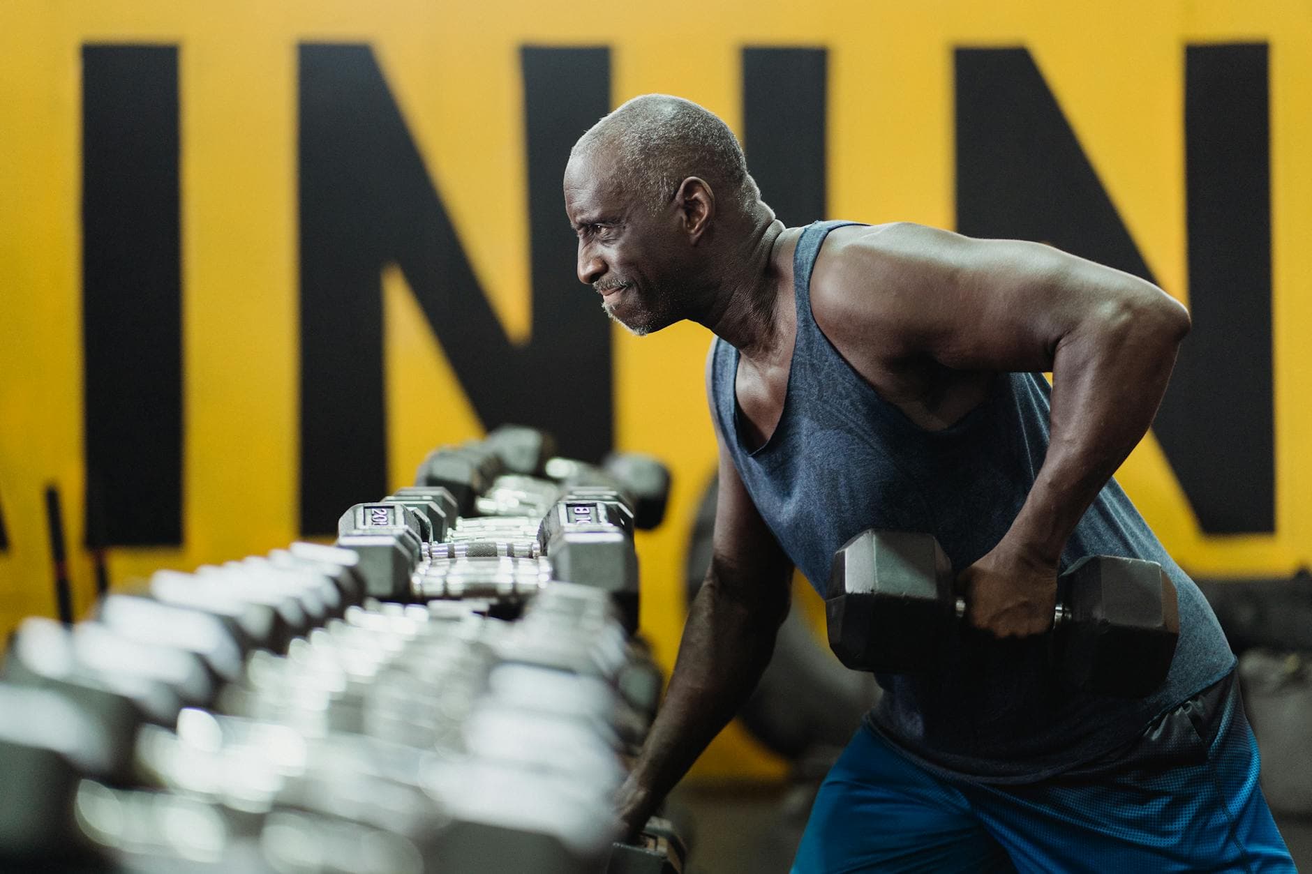 Strong senior man focusing on strength training with dumbbells in a vibrant gym. - resistance training benefits