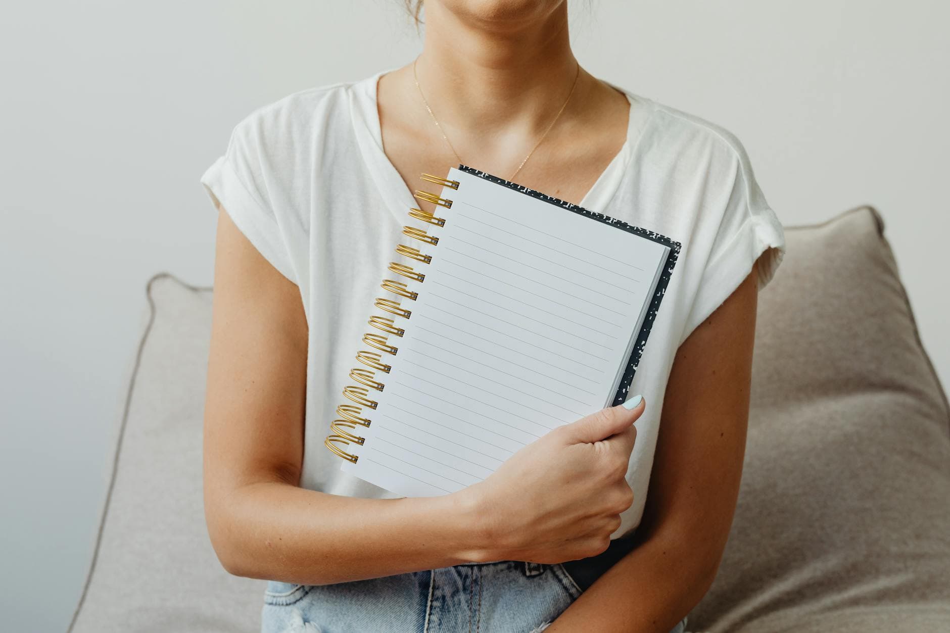 Woman holding an open blank spiral notebook wearing a white top in a cozy indoor setting. - spring reset journal prompts