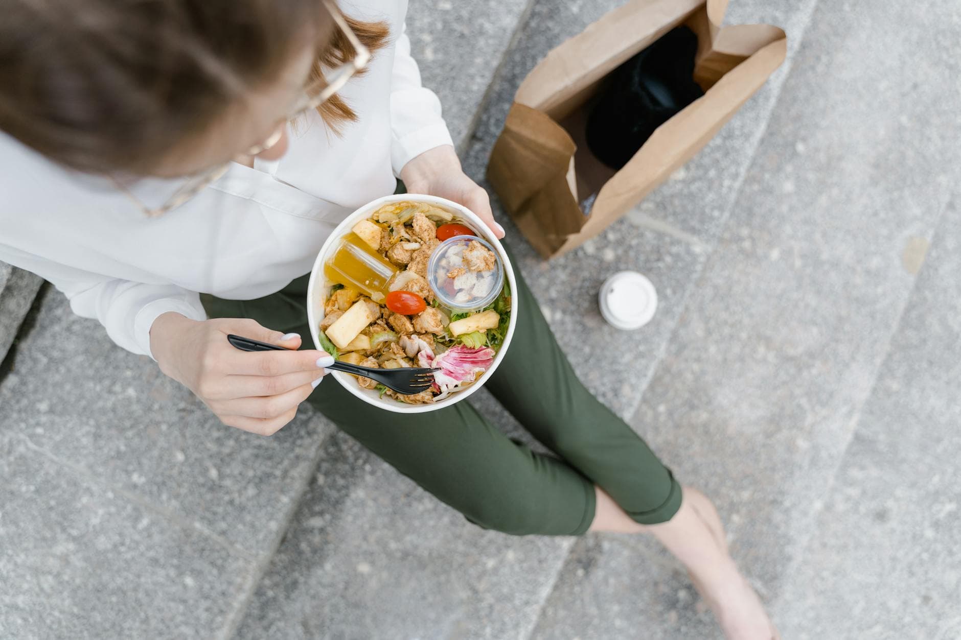 Top-down view of a woman enjoying a healthy salad outdoors during a casual lunch break. - healthy lunch prep