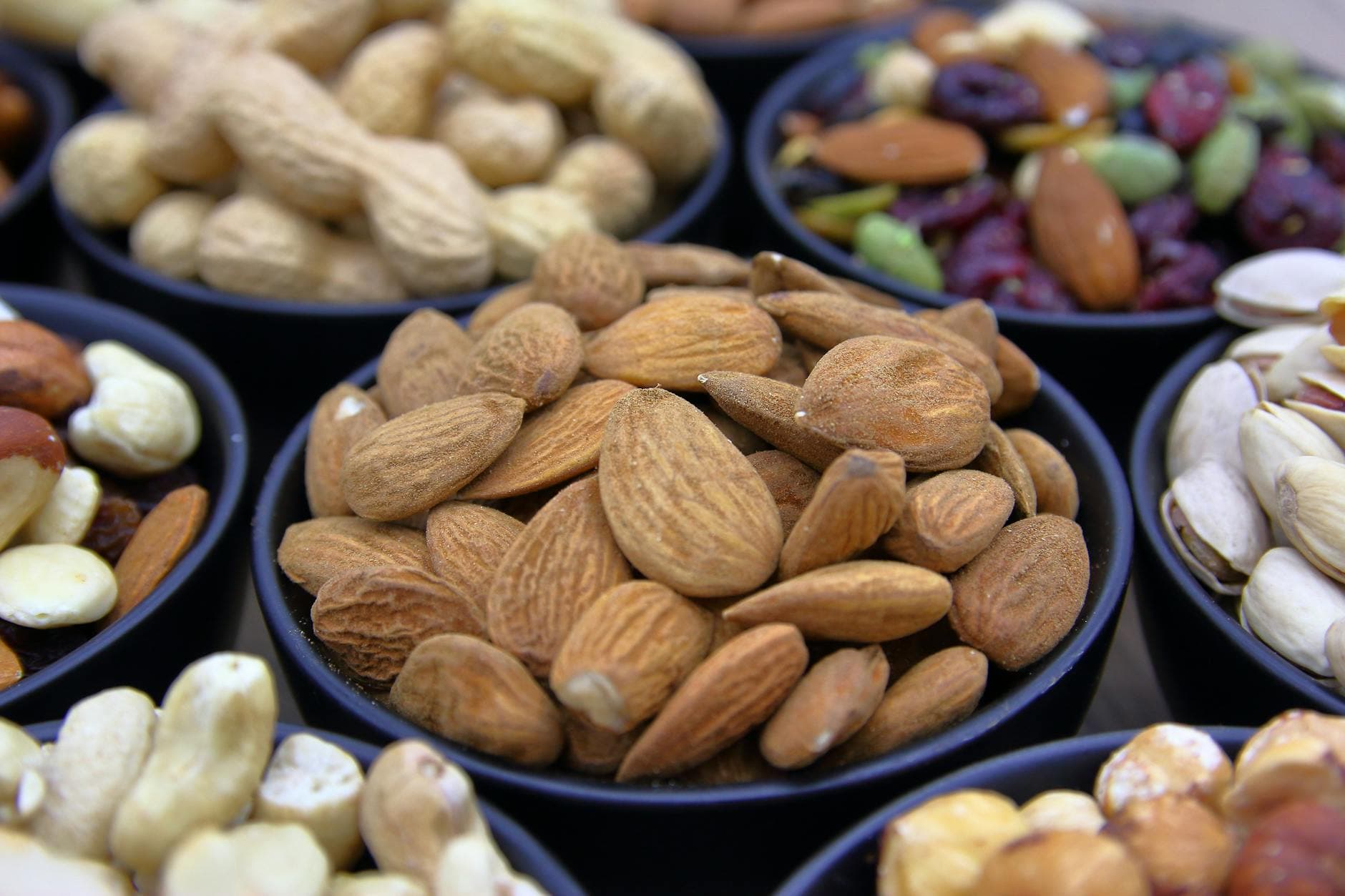 Collection of assorted nuts and dried fruits in black bowls, showcasing colorful and healthy snacks. - hiking trail snacks