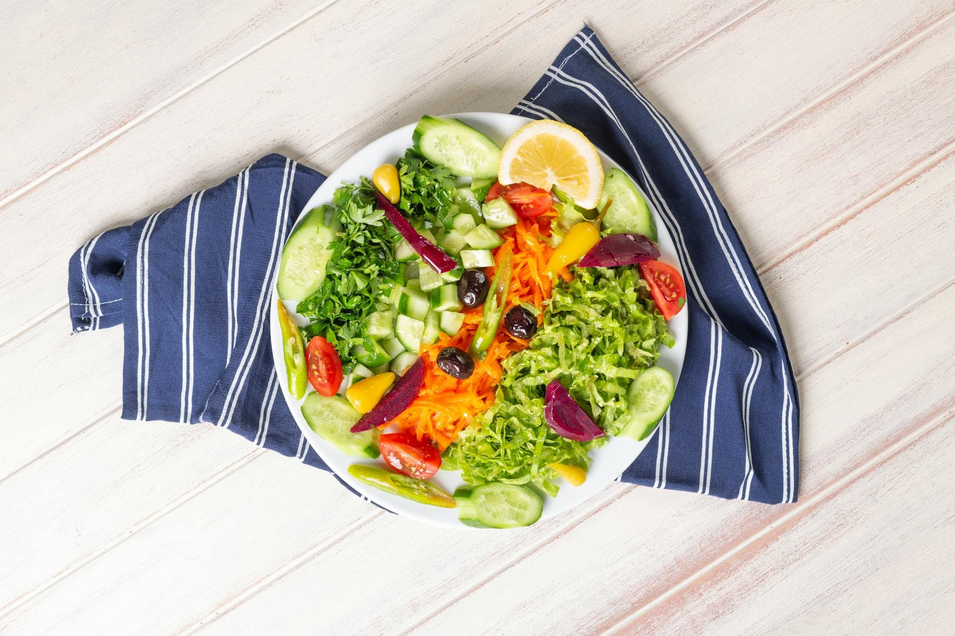 A colorful and fresh salad with assorted vegetables, lemon slice, and olives on a plate. - mediterranean dash diet