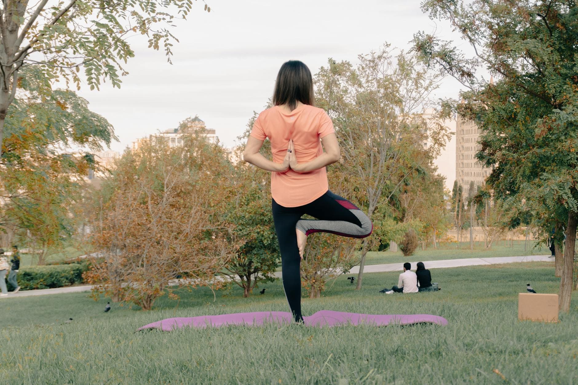 Adult woman performing yoga on a mat in a park, surrounded by greenery and trees. - nutrient timing fitness