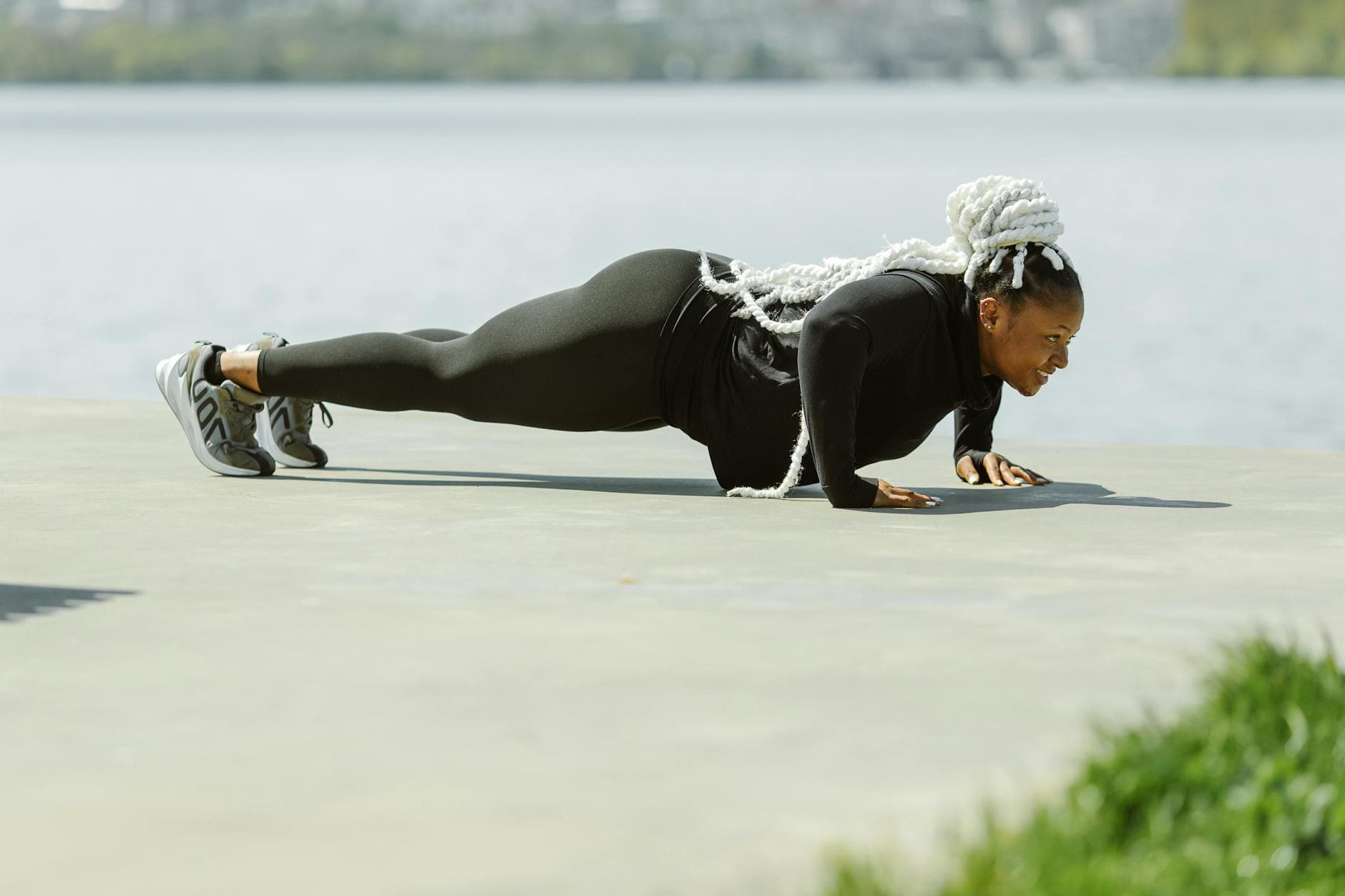 Black woman performing push-ups outdoors near water, promoting active lifestyle and fitness. - outdoor cardio beginners