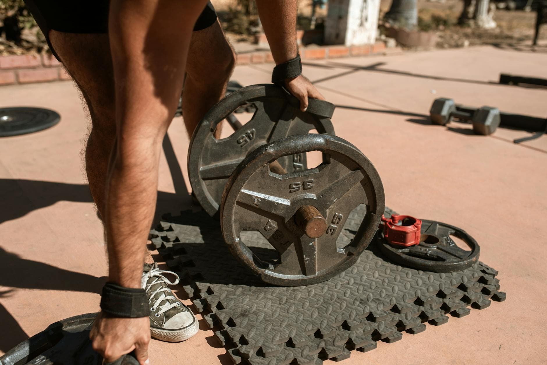 A man adjusts weight plates on a barbell during an outdoor workout session. - outdoor strength training