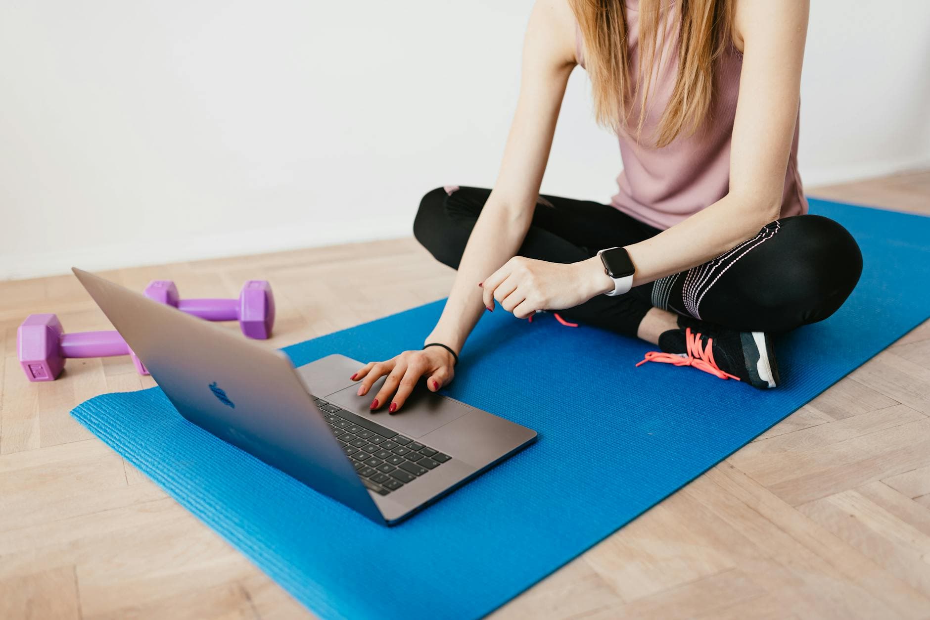 Faceless female in activewear sitting on blue yoga mat on floor and browsing laptop - quick at home workouts