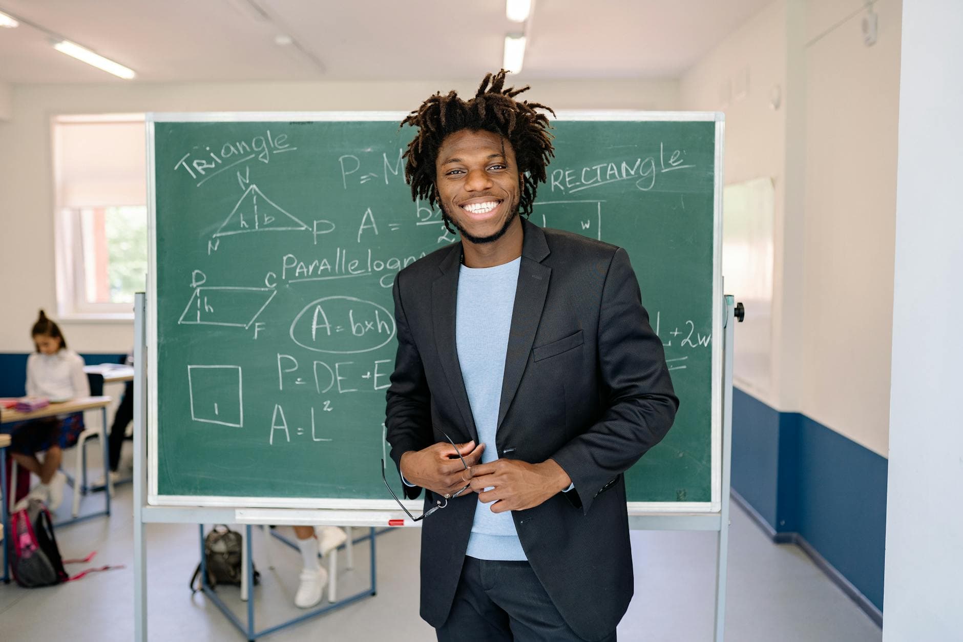 A cheerful teacher stands by the chalkboard in a classroom, illustrating math concepts. - spring cravings explained