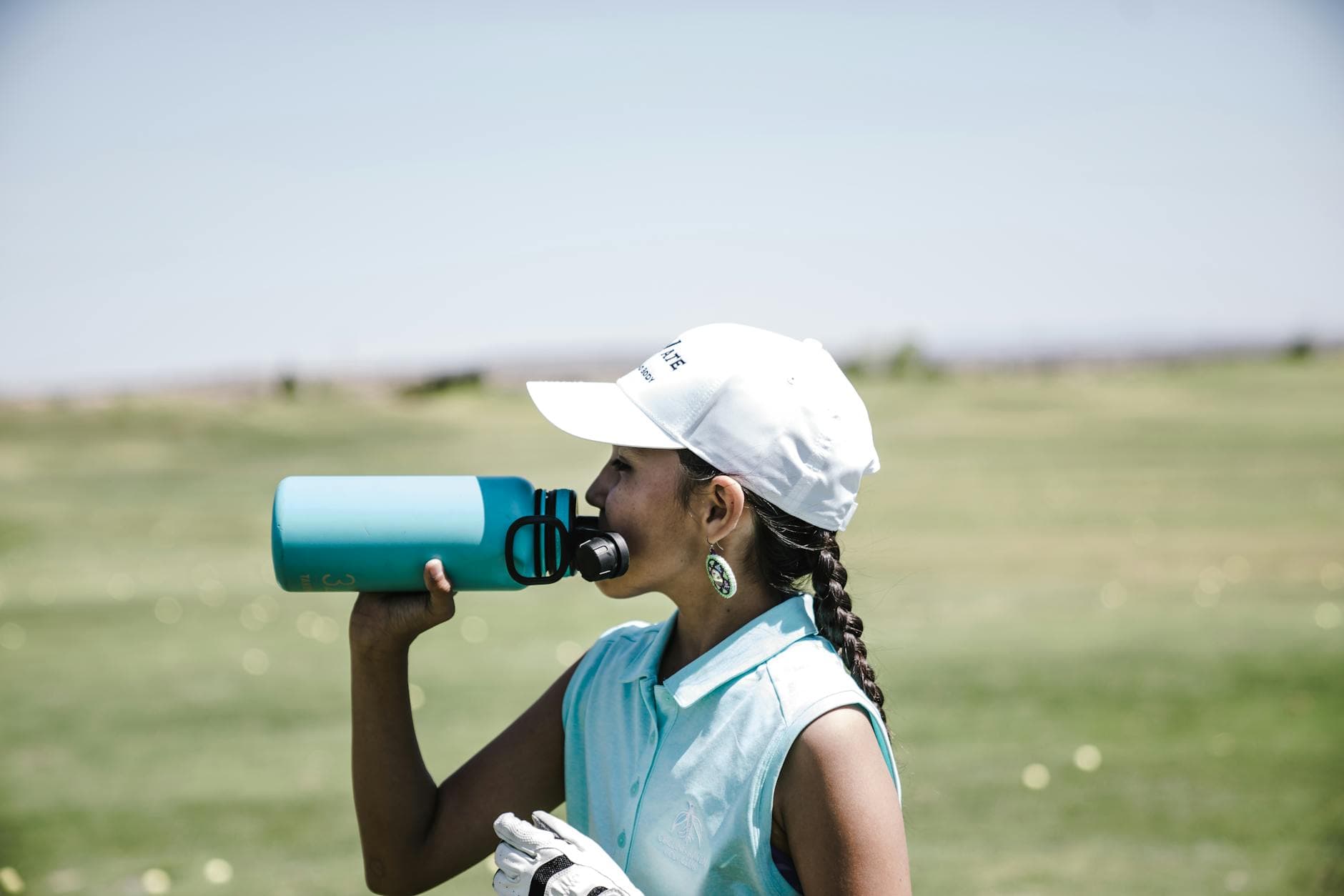 Woman golfer taking a break to hydrate on a sunny day in a field. - spring sports hydration