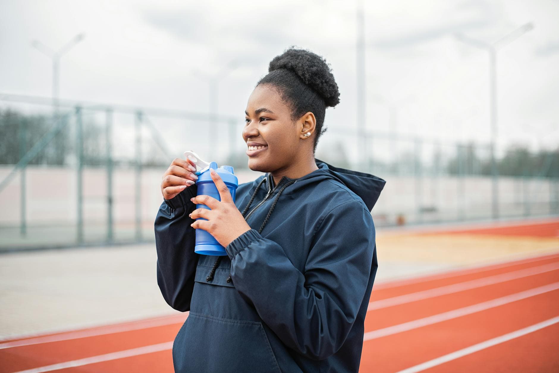 Smiling woman in sports attire holding a water bottle on an outdoor track, enjoying a break. - spring training hydration