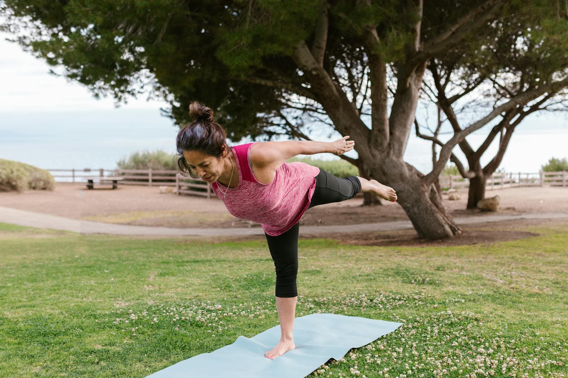 Woman in a balancing yoga pose on a mat in a scenic outdoor park setting. - spring yoga renewal