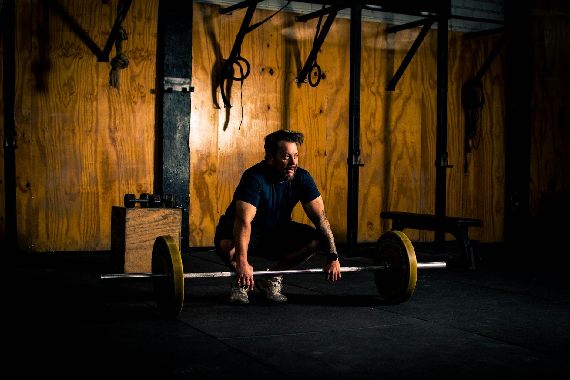 A man prepares to lift a barbell in a dimly lit gym environment, focusing on strength training. - best core workout routine